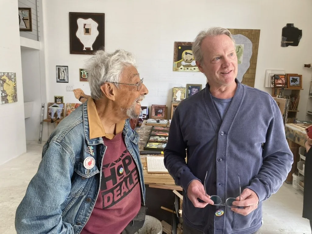 Two men stand next to each other in mid-conversation, looking at something off-camera