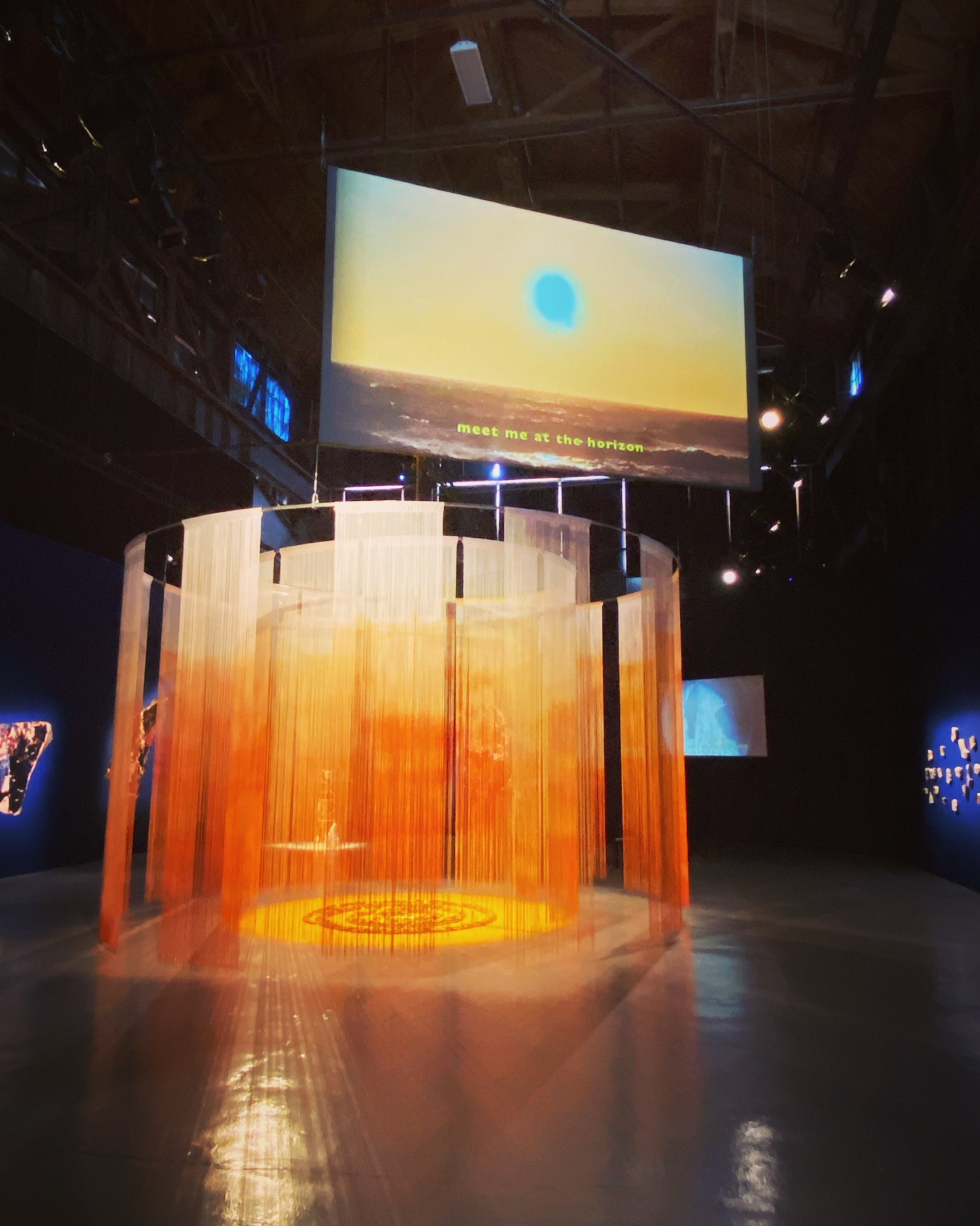 Art installation with a large TV screen and round display of long, orange-yellow hanging material