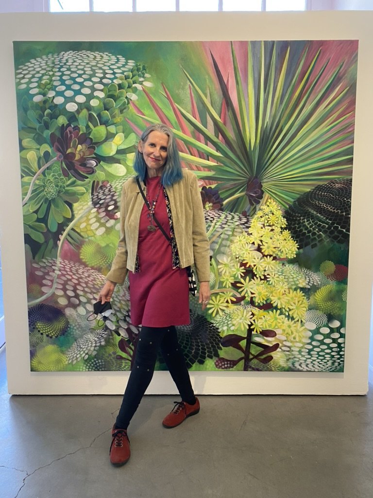Artist standing and smiling in front of artwork