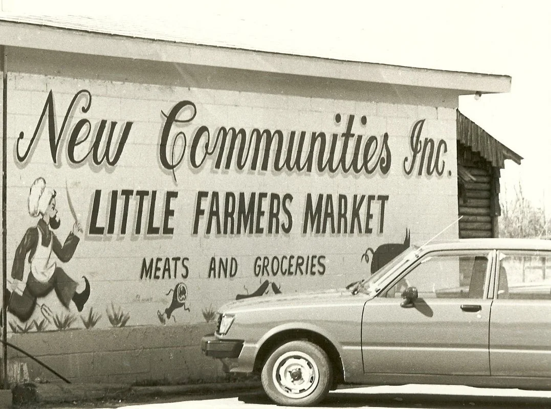 Black and white image of a painted mural on the side of a building that reads New Communities Inc. Little Farmer's Market meat and groceries