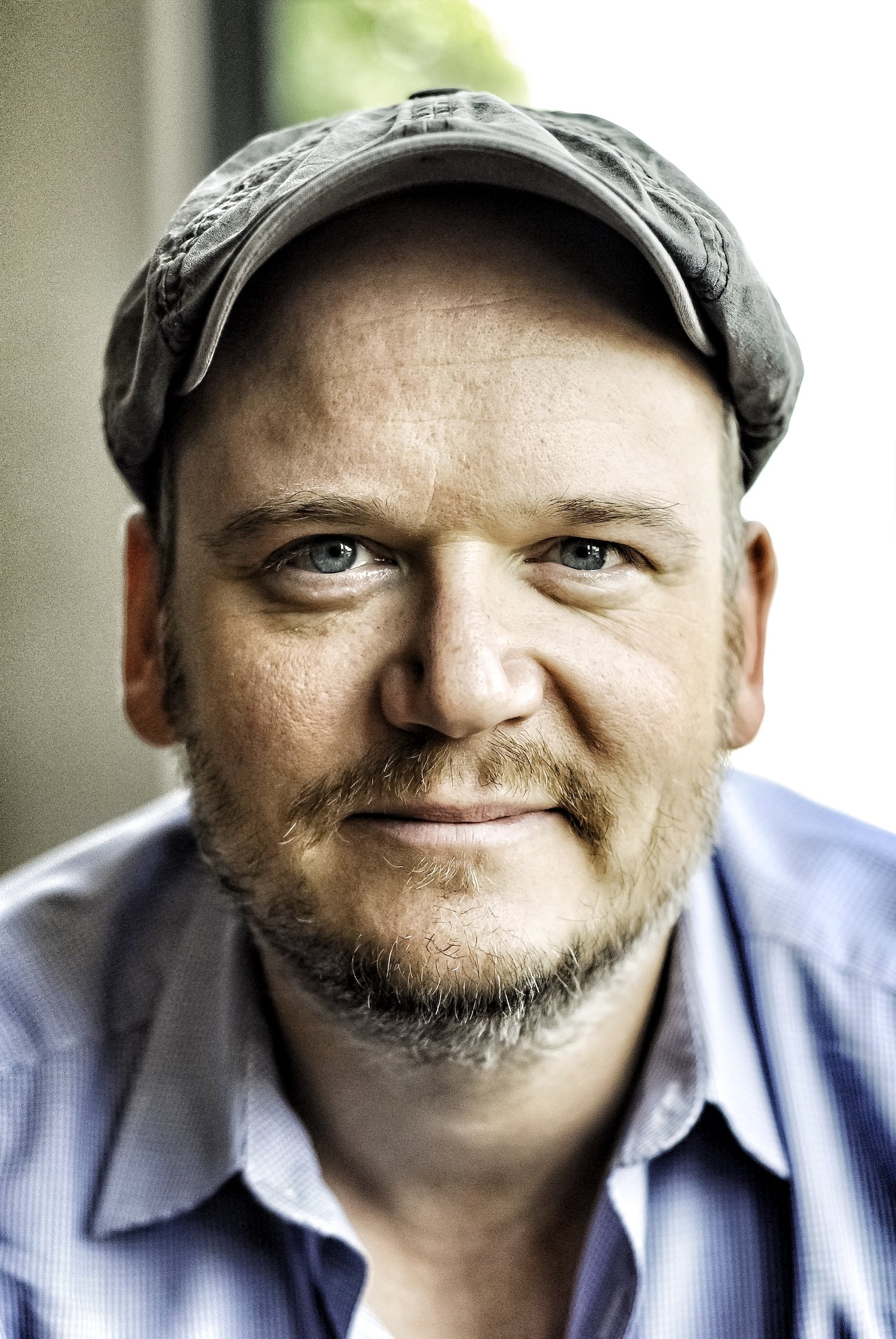 Nahaufnahme eines Mannes mit grauem Cap, blauen Augen, Bart, trägt ein kariertes Hemd.