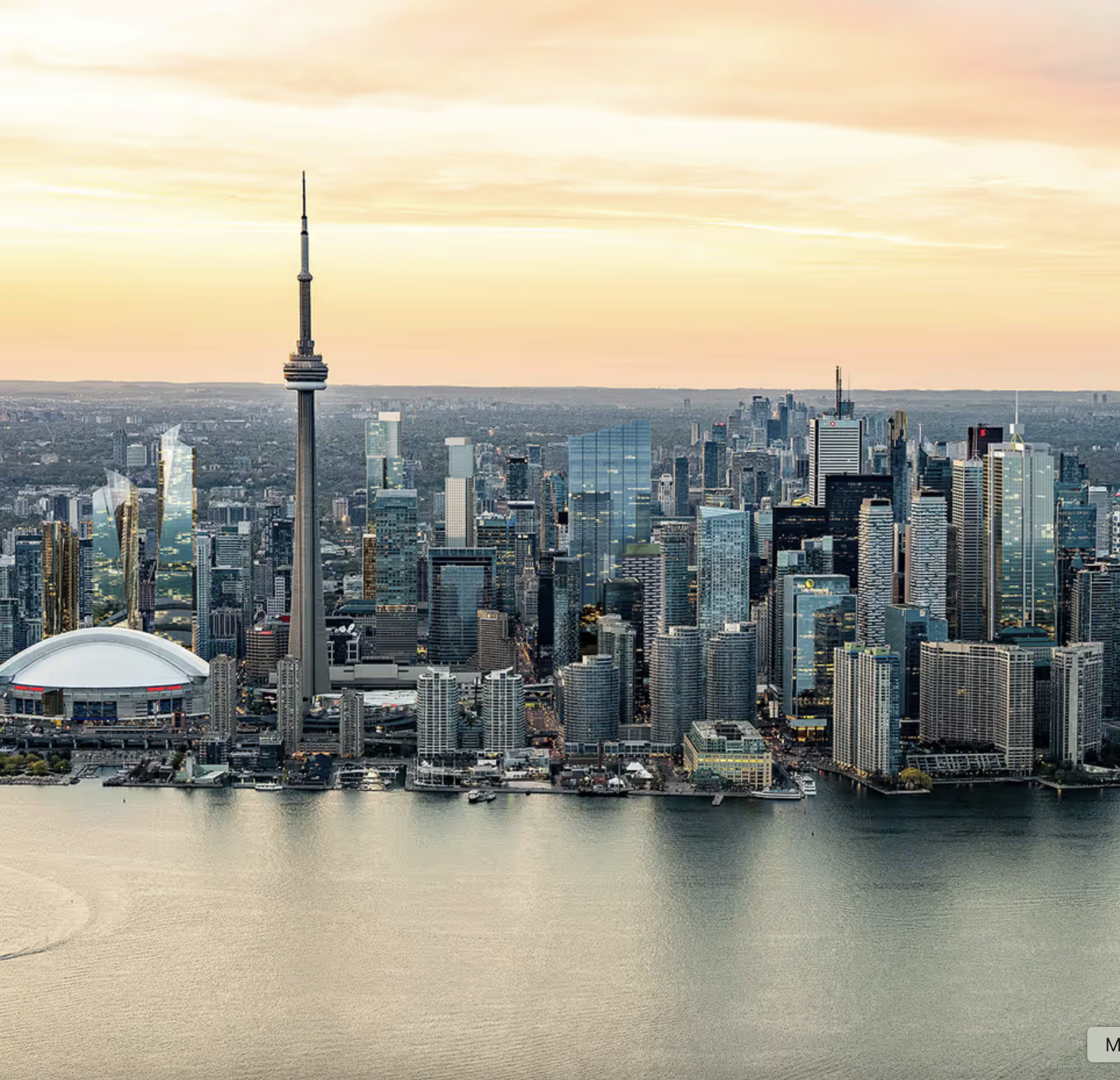 Aerial view of downtown Toronto with the CN Tower, modern skyscrapers, and Lake Ontario at sunset.