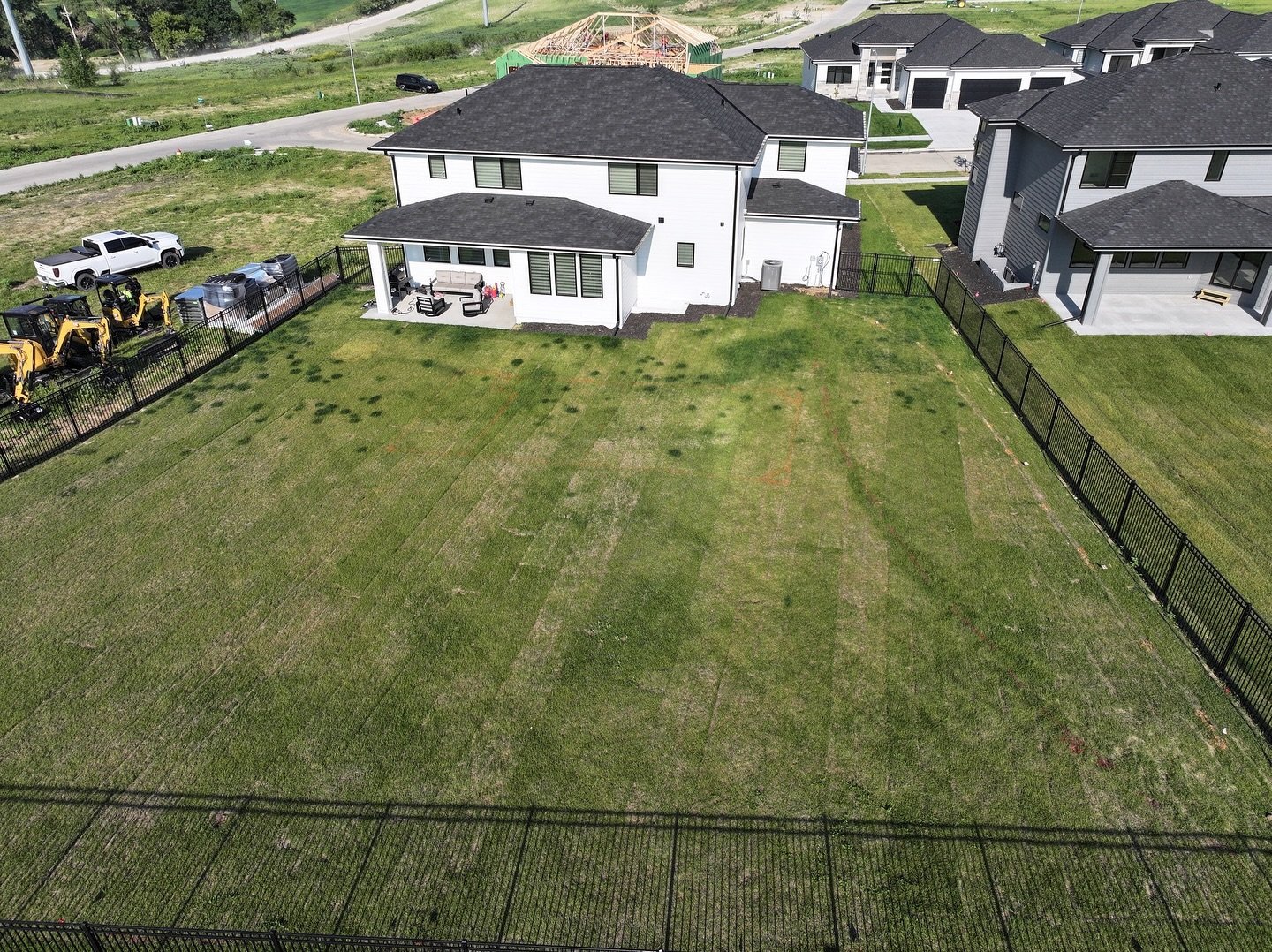 Backyard with a house, patio furniture, and a fenced yard, neighboring other houses, with construction and vehicles nearby.