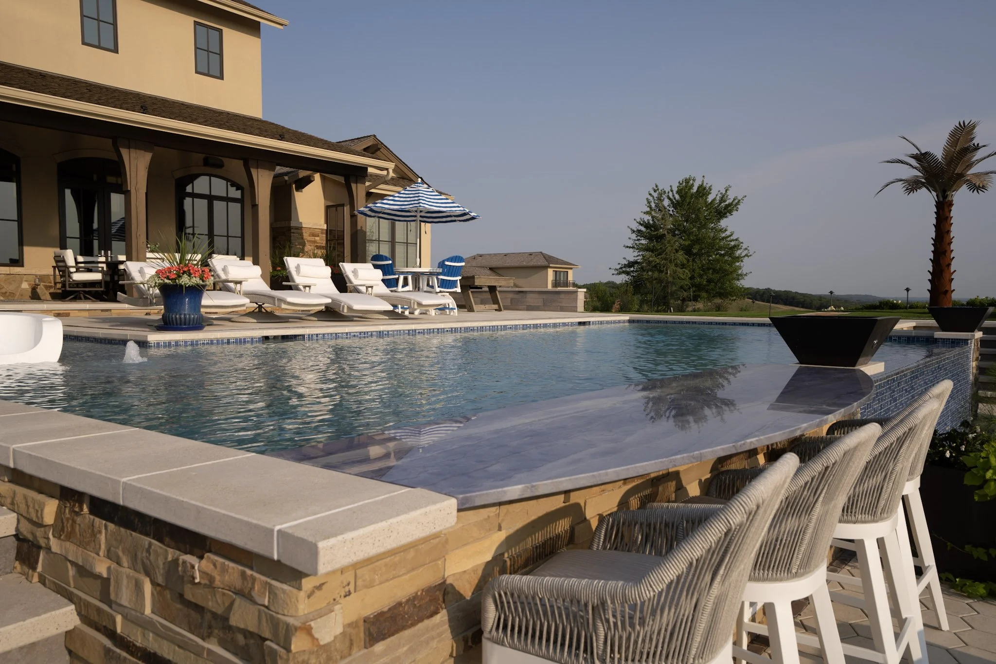 Luxury backyard with a swimming pool, lounge chairs, a large house, and outdoor furniture.