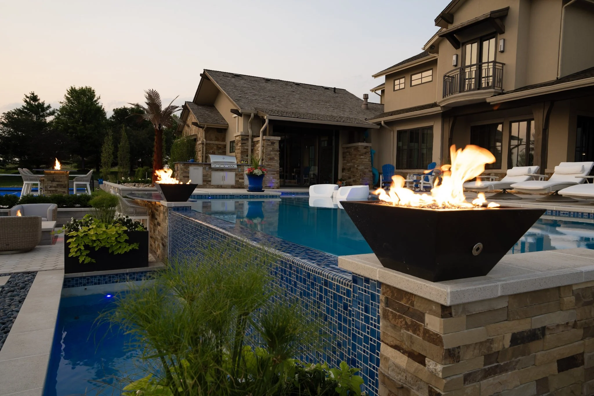 Luxurious backyard with a swimming pool, outdoor fire pits, lounge chairs, and a modern house in the background.
