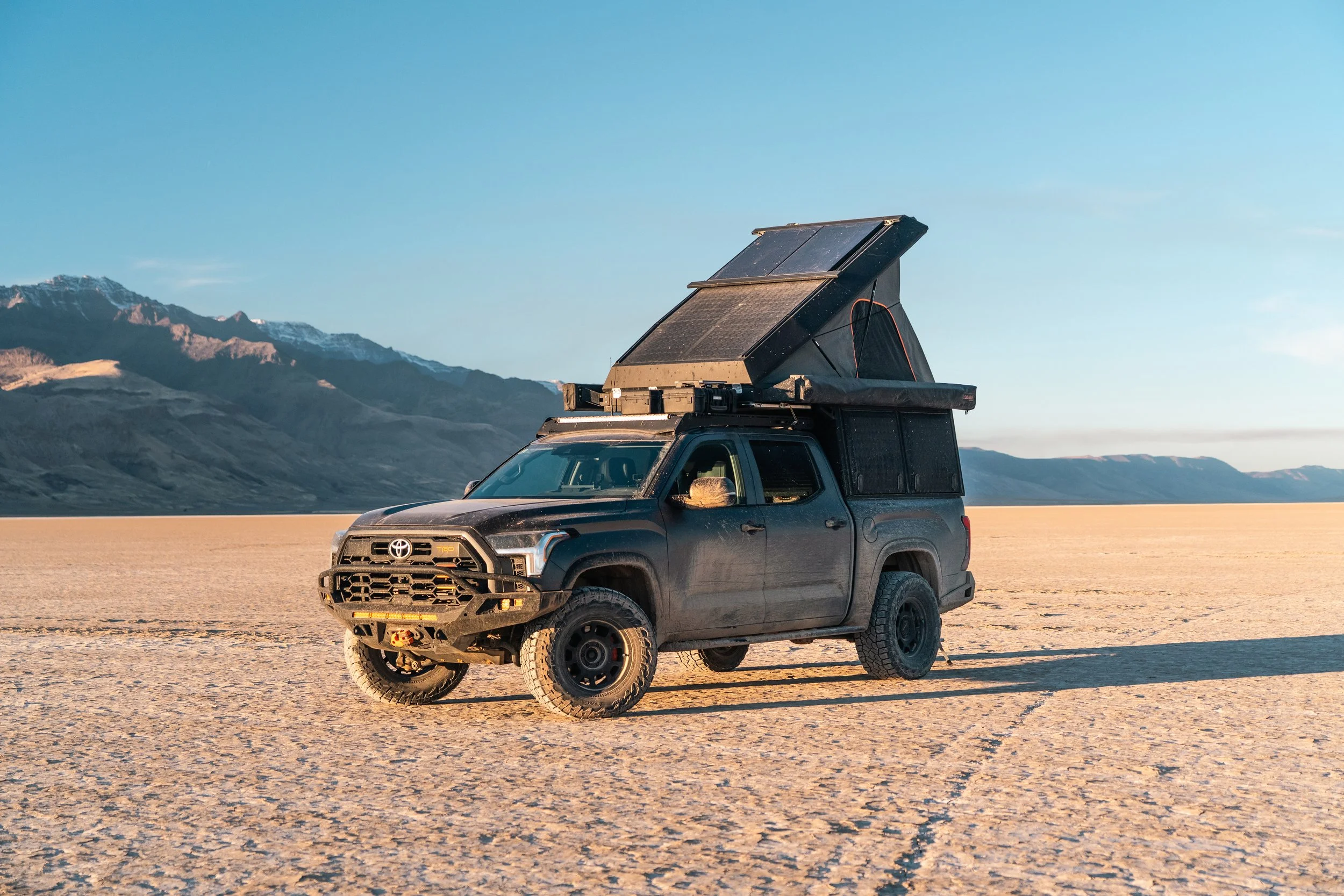 A black Toyota off-road vehicle with a rooftop tent in a desert landscape with mountains in the background.