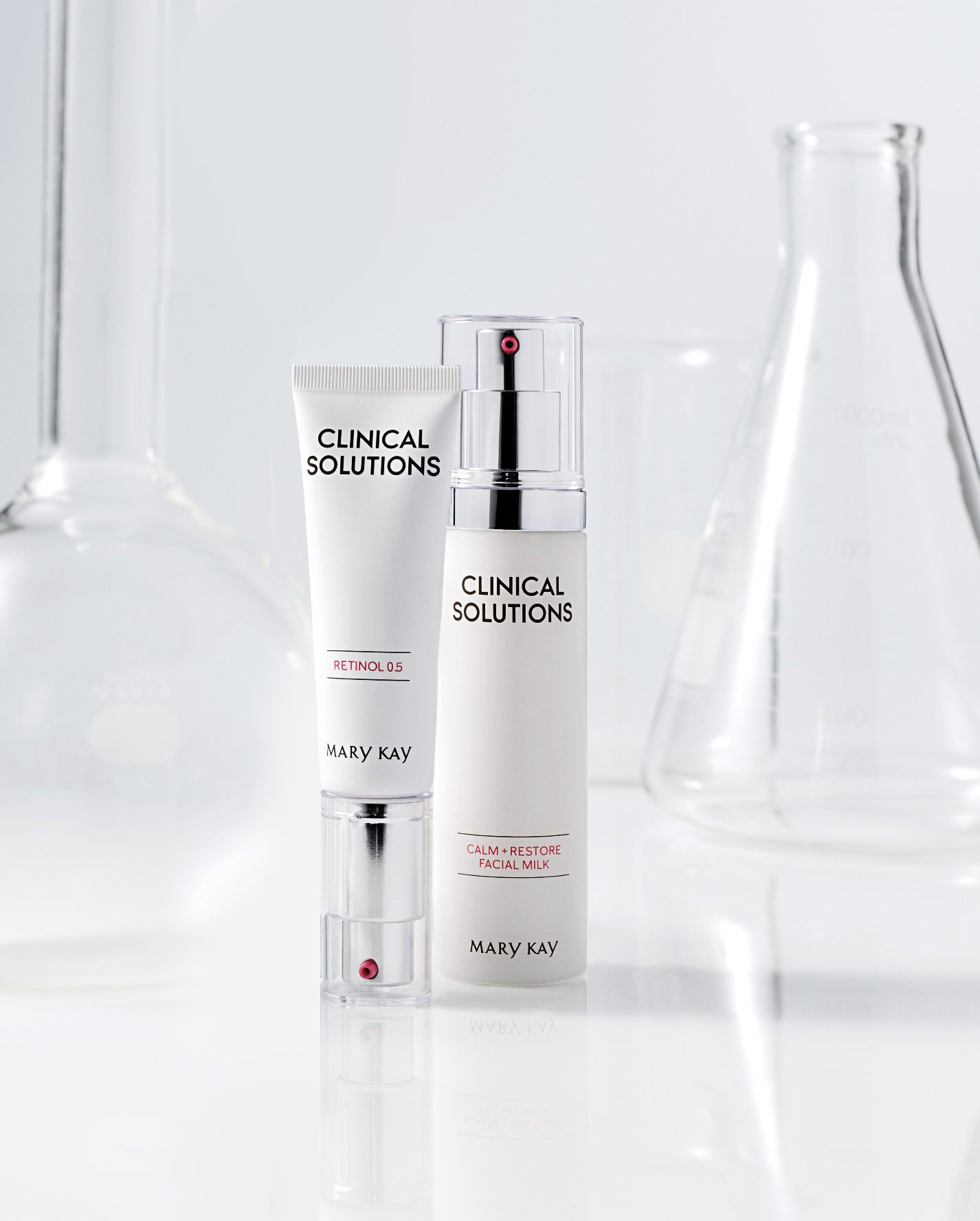 Mary Kay Clinical Solutions skincare products, including retinol 0.5 and calm restore facial milk, on a white surface with glass lab equipment in the background.