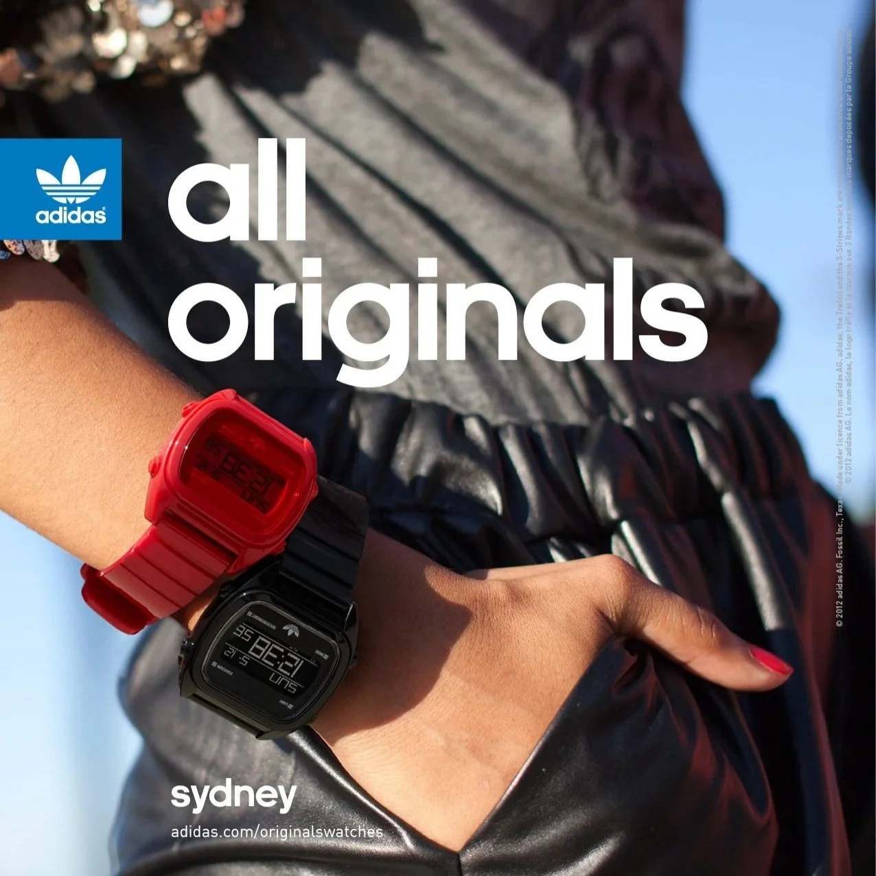 A person's wrist wearing two digital watches, one red and one black, with a background of a gray and black striped fabric and a black leather garment. The text overlay reads 'adidas all originals' and 'sydney' with a website link.