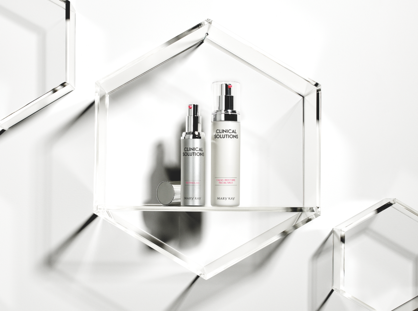Two skincare bottles labeled 'Clinical Solutions' and 'Mary Kay' placed inside a clear geometric display case with mirrors, on a white background.