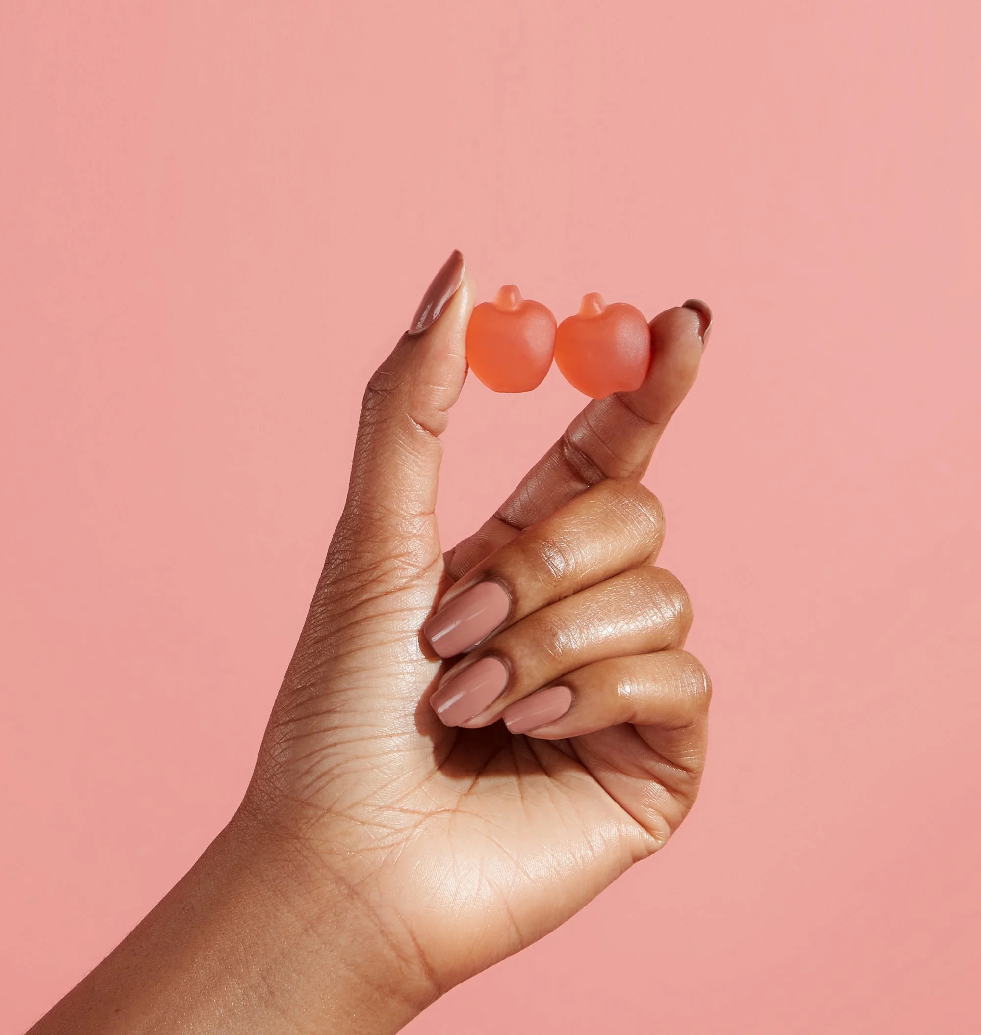 A hand holding two small pink gummy candies shaped like bear heads against a pink background.