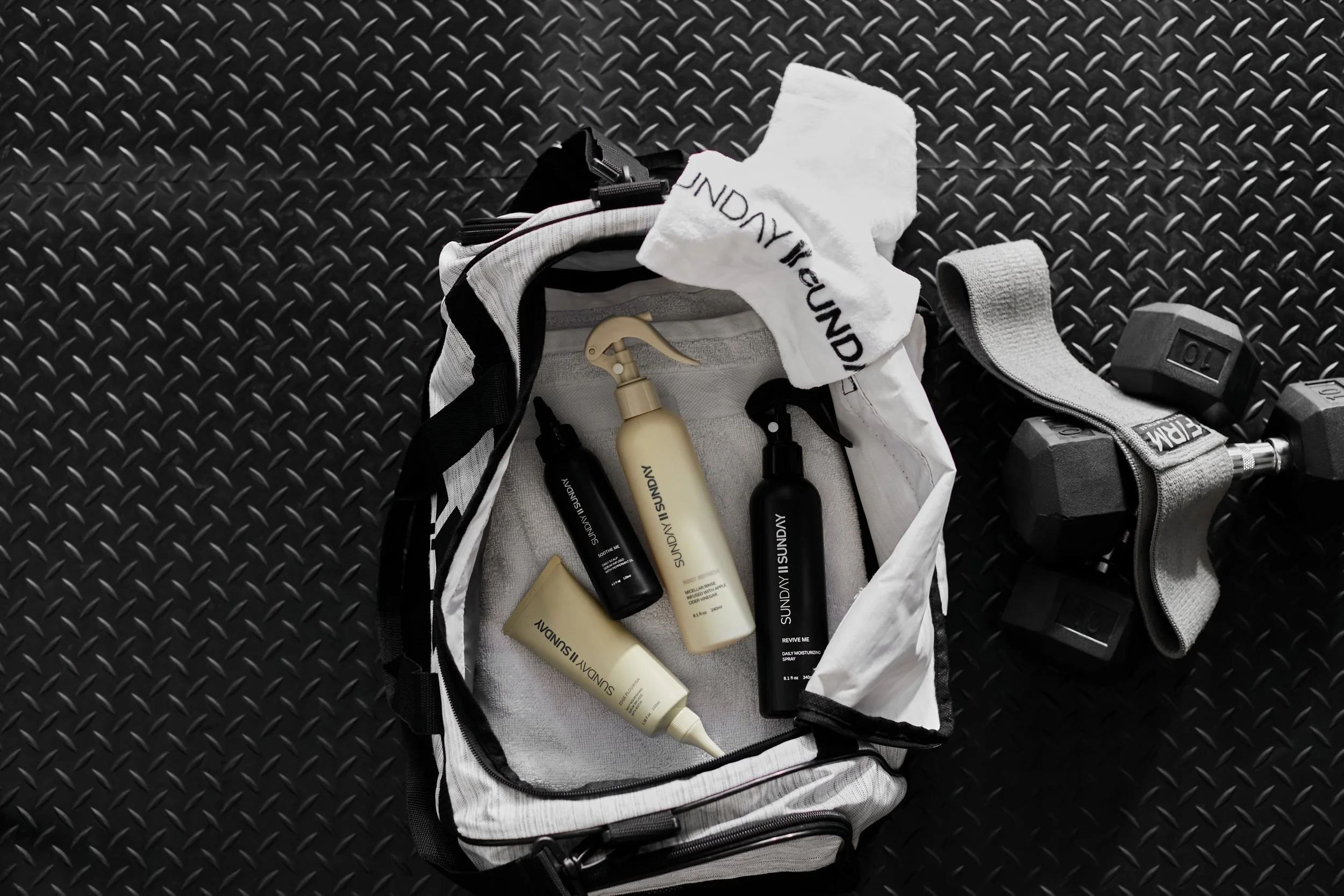 Sports bag and dumbbells on a textured gym floor with skincare products and a towel inside the bag.