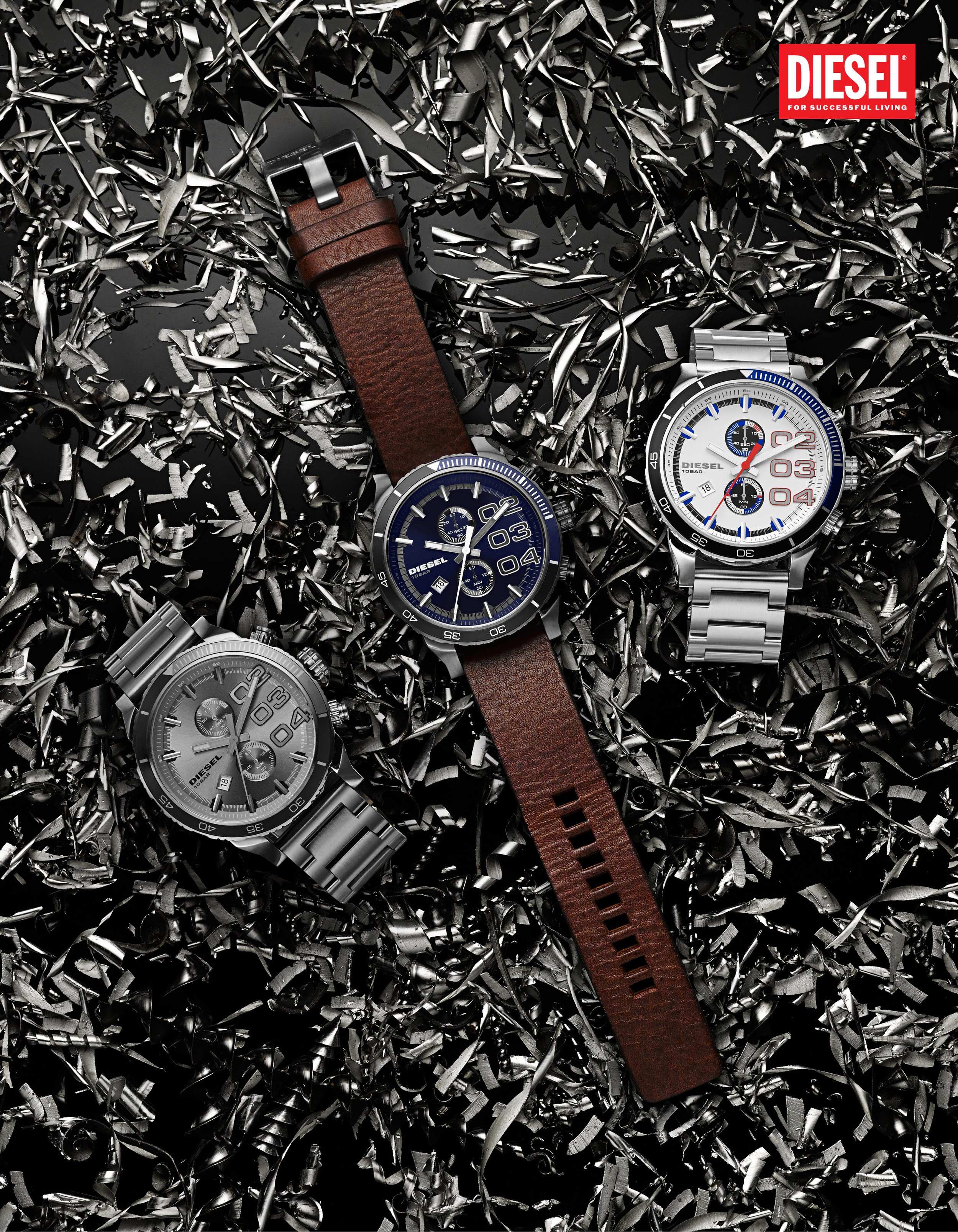 A display of four Diesel watches with different styles and colors, arranged on a bed of shiny metallic shavings, with a Diesel logo in the top right corner.