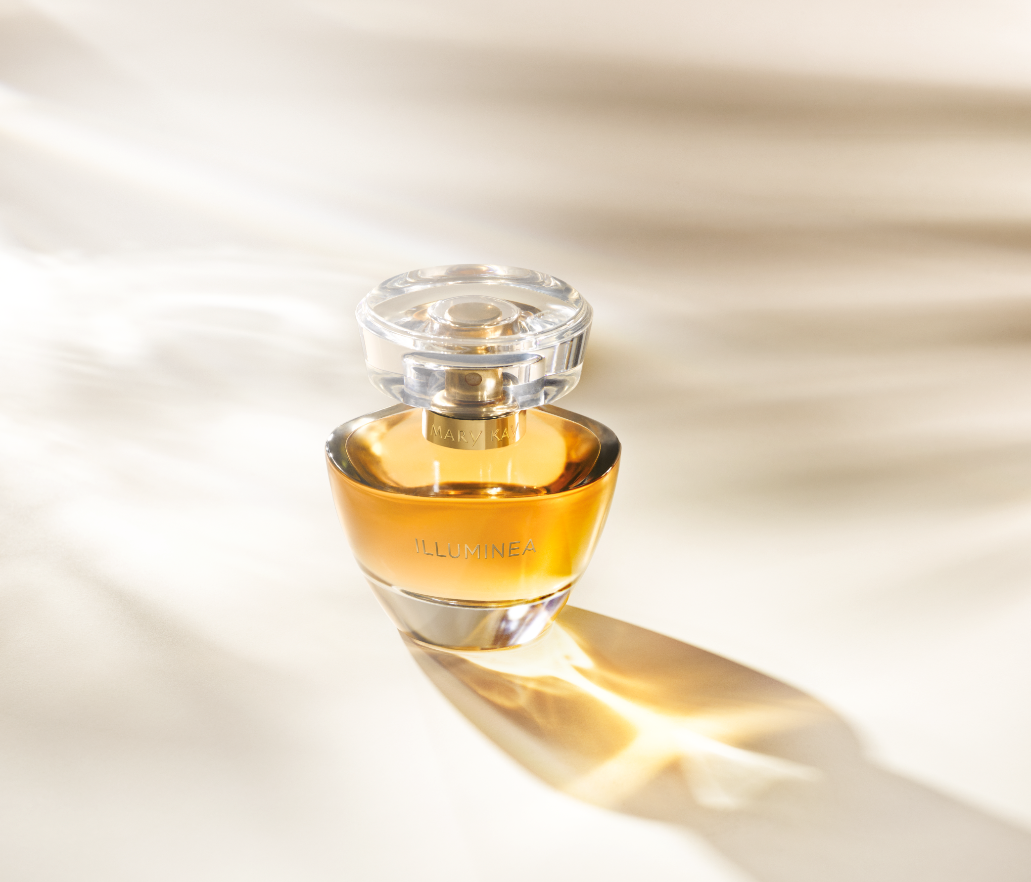 A glass perfume bottle labeled 'ILLUMINEA' with a clear cap, placed on a light surface with soft shadows.