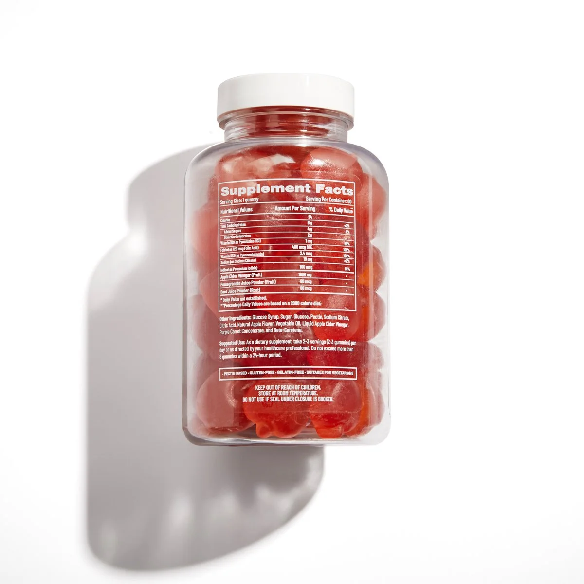 A clear plastic jar filled with red gummy candies. The jar has a white lid and a red label with supplement facts, ingredients, and usage instructions printed on it.