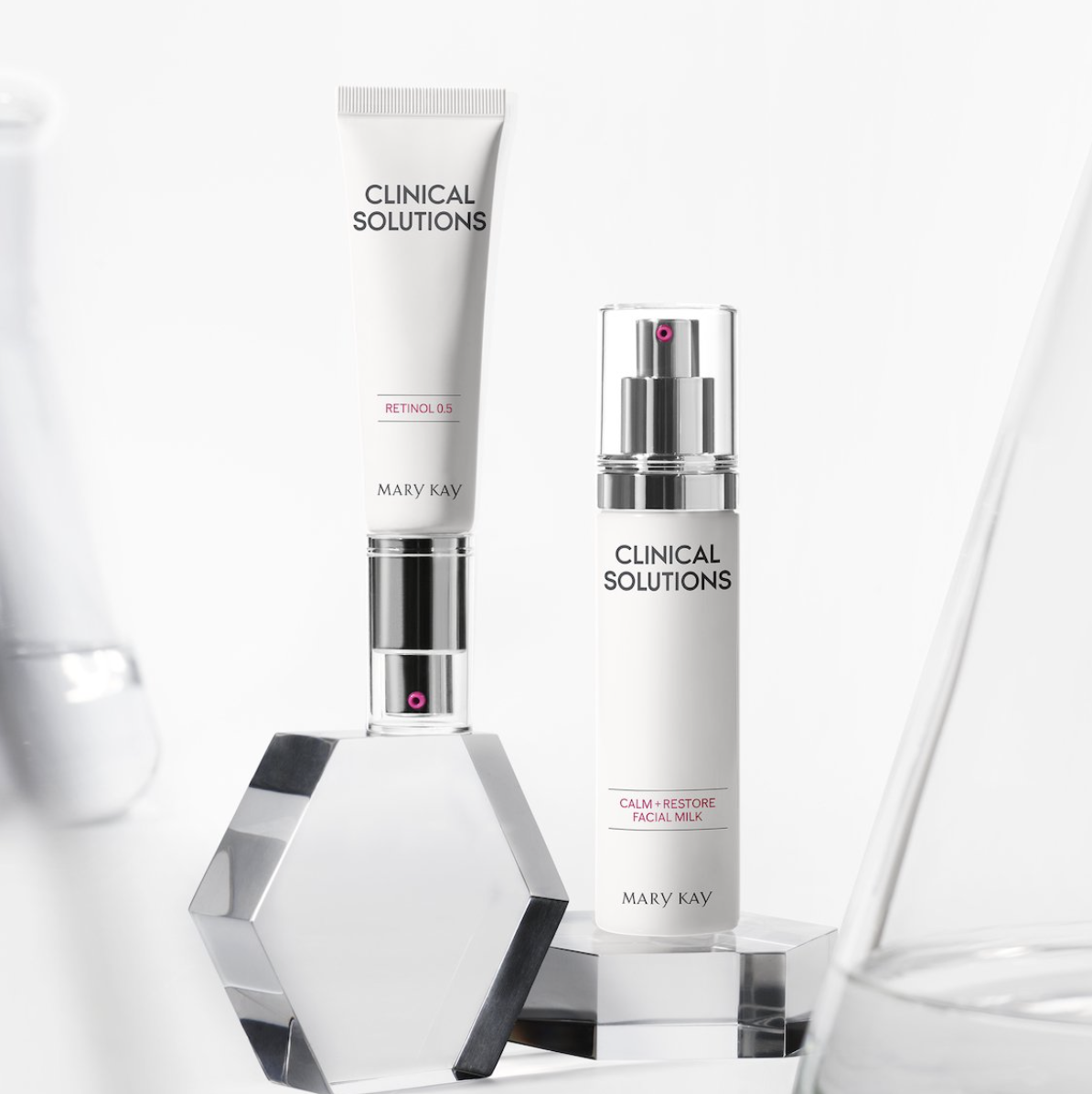Mary Kay skincare products from the Clinical Solutions line, including Retinol 0.5 and Calm + Restore Facial Milk, displayed on a reflective surface with a crystal stand, against a white background.