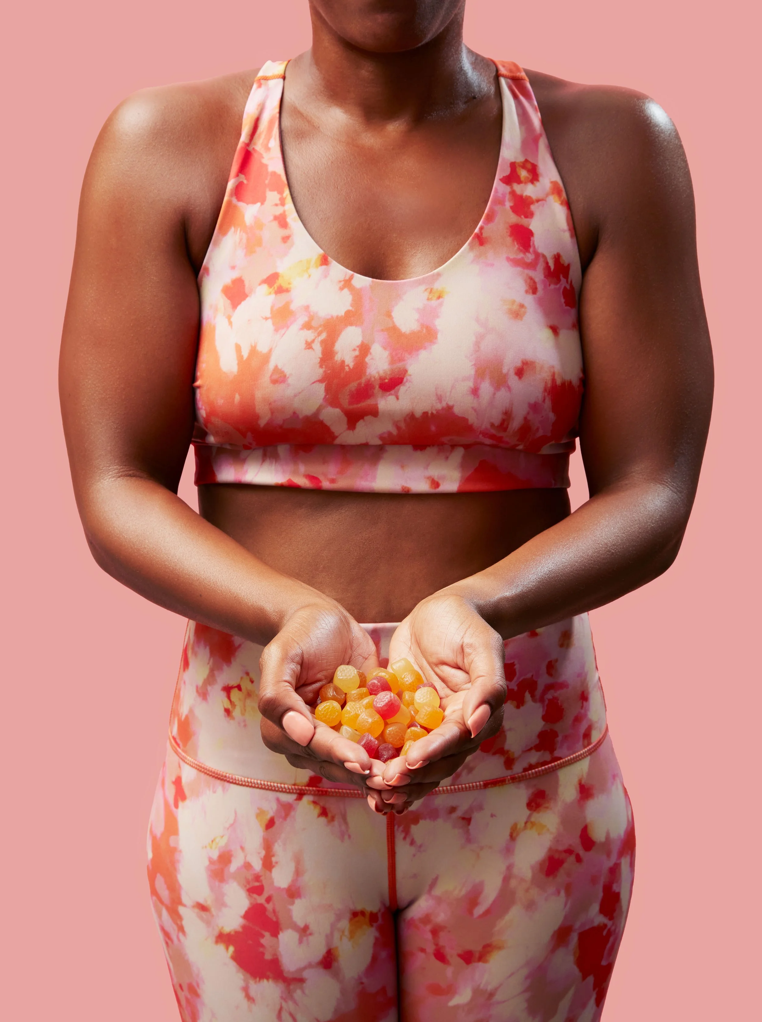 A woman wearing pink and white tie-dye workout clothing, holding a handful of colorful jelly beans against a pink background.