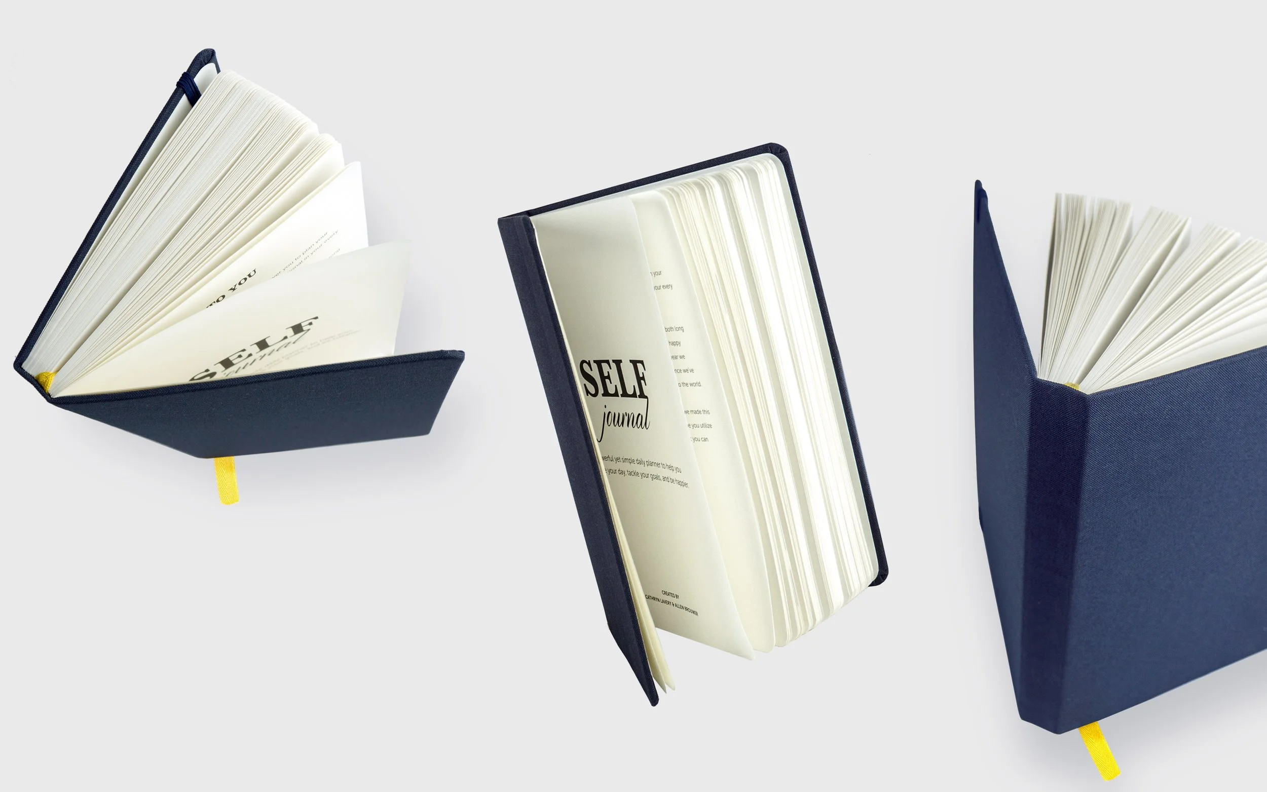 Three closed hardcover notebooks with black covers and yellow bookmarks, each opened to reveal pages, on a white background.
