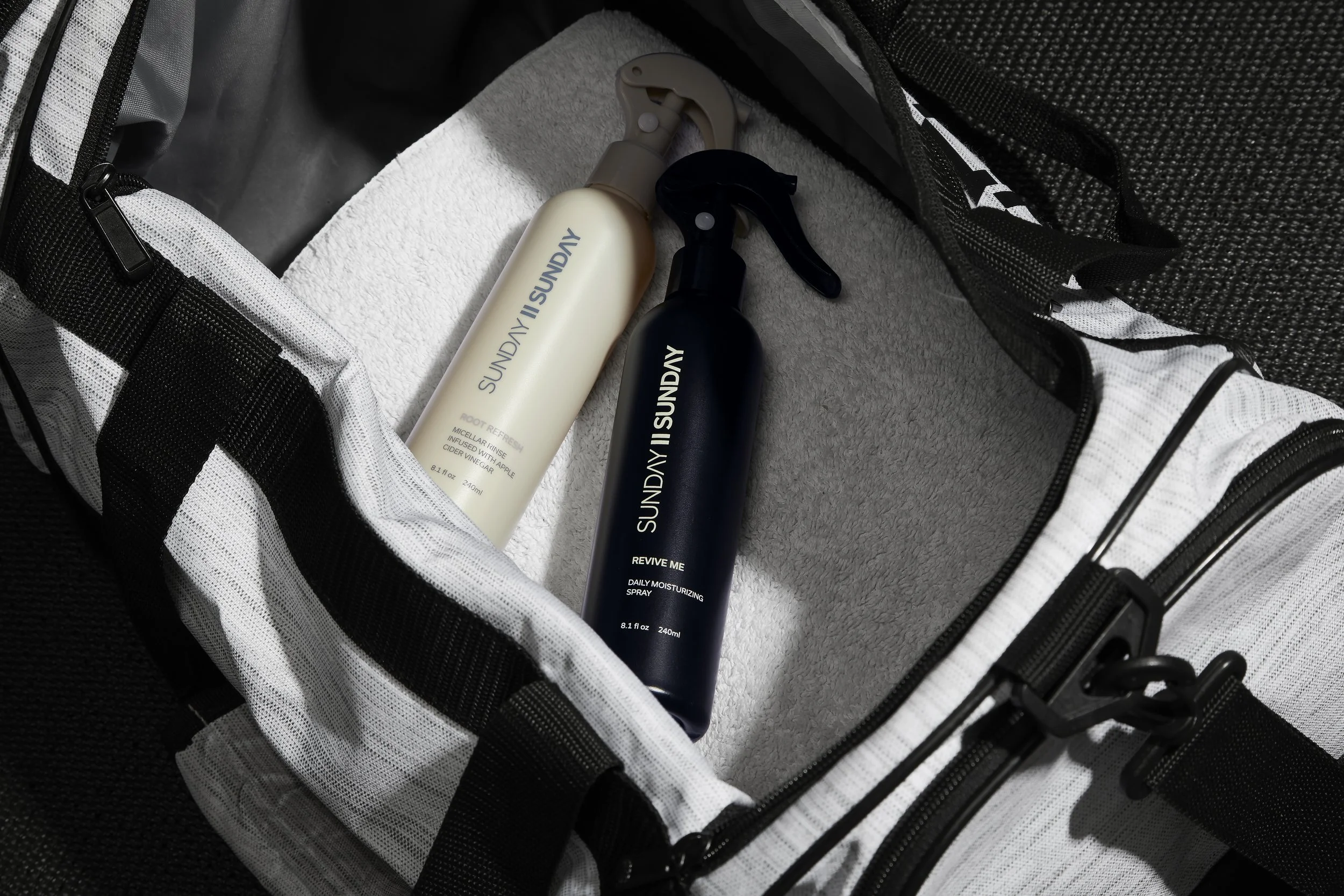 Two spray bottles labeled 'SUNDAY' in a white and black backpack. One bottle is beige and the other is black, both with spray nozzles.