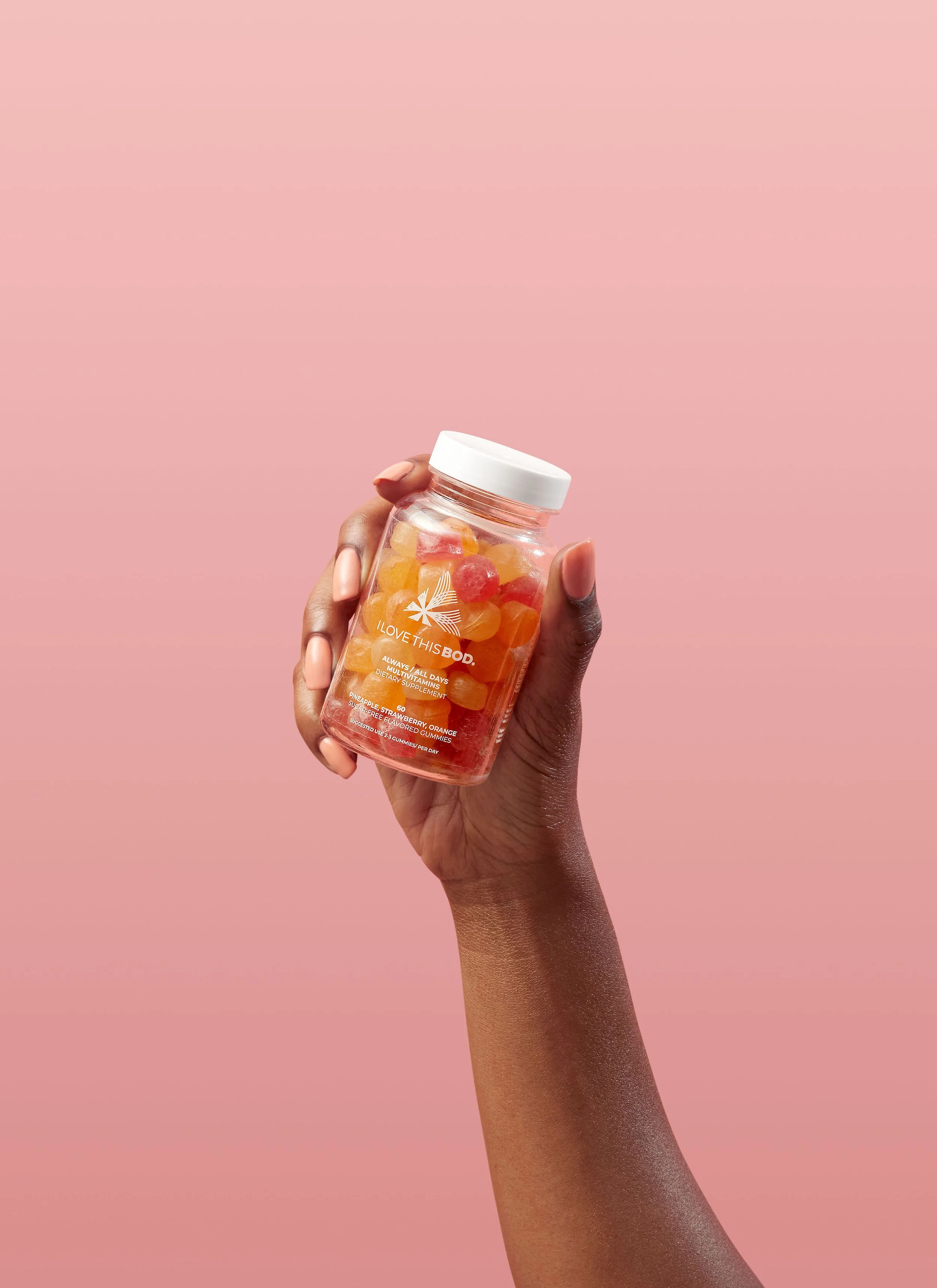 Hand holding a jar of gummy vitamins with pink and yellow gummies inside, against a pink background.