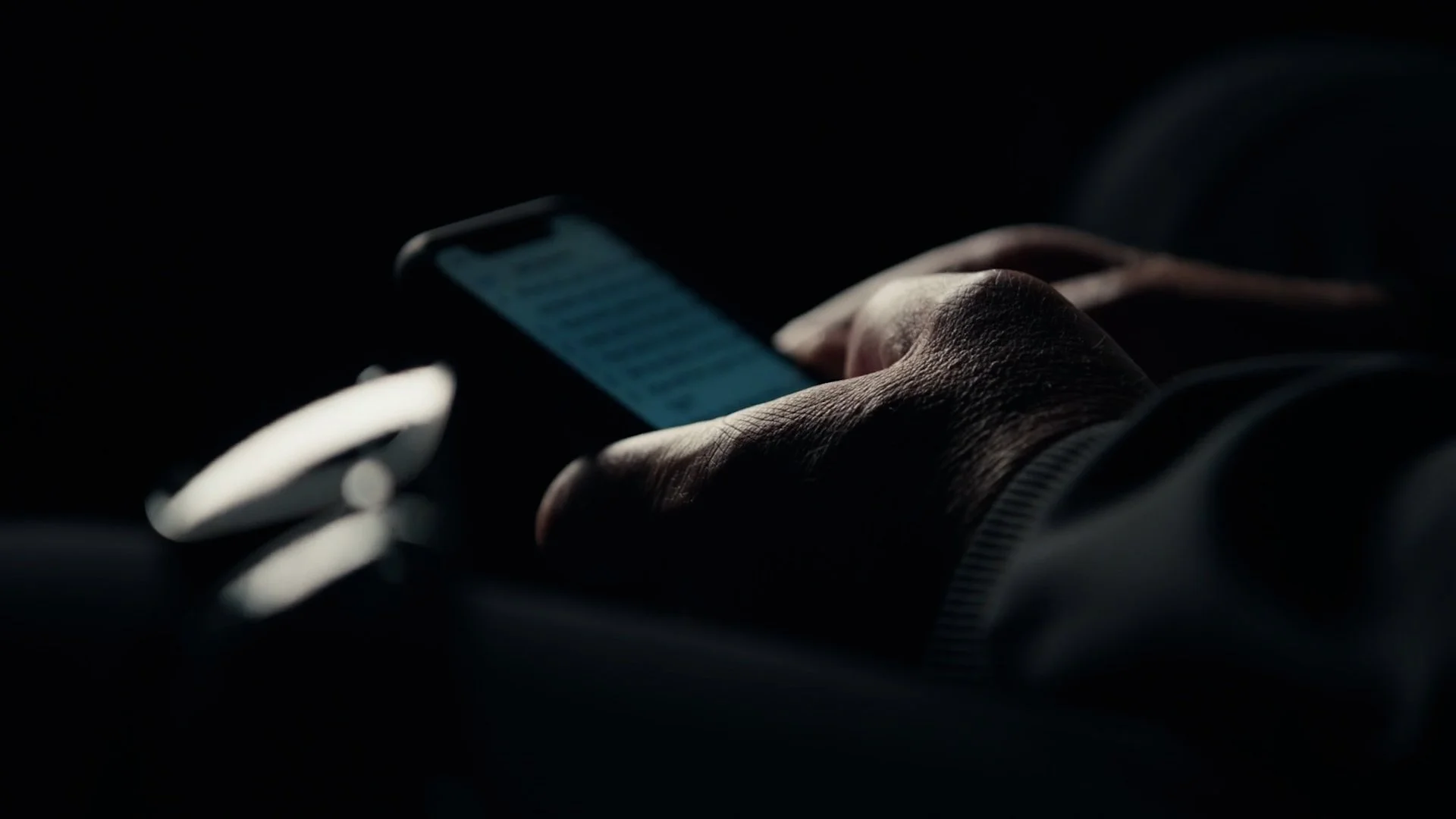 Close-up of a person's hand holding a smartphone in a dark environment, with text messages visible on the screen.