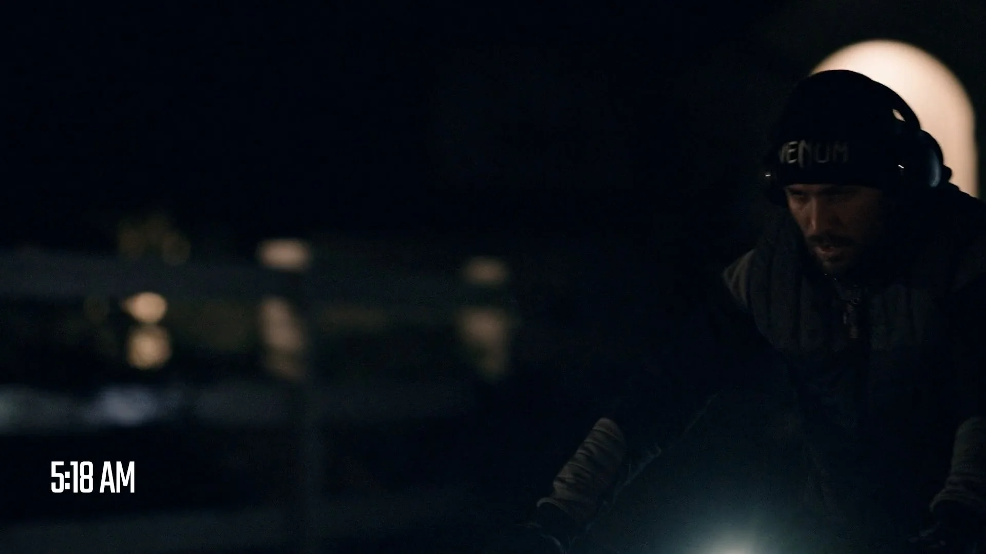 A man in a black helmet and jacket riding a motorcycle at dawn or early morning, with the timestamp 5:18 AM displayed in the lower left corner.