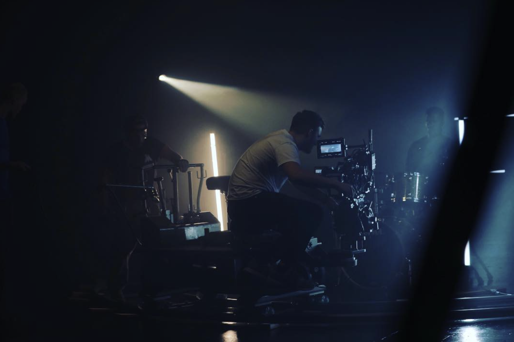 Filmmaking crew operating camera equipment on set with dim lighting and a spotlight.
