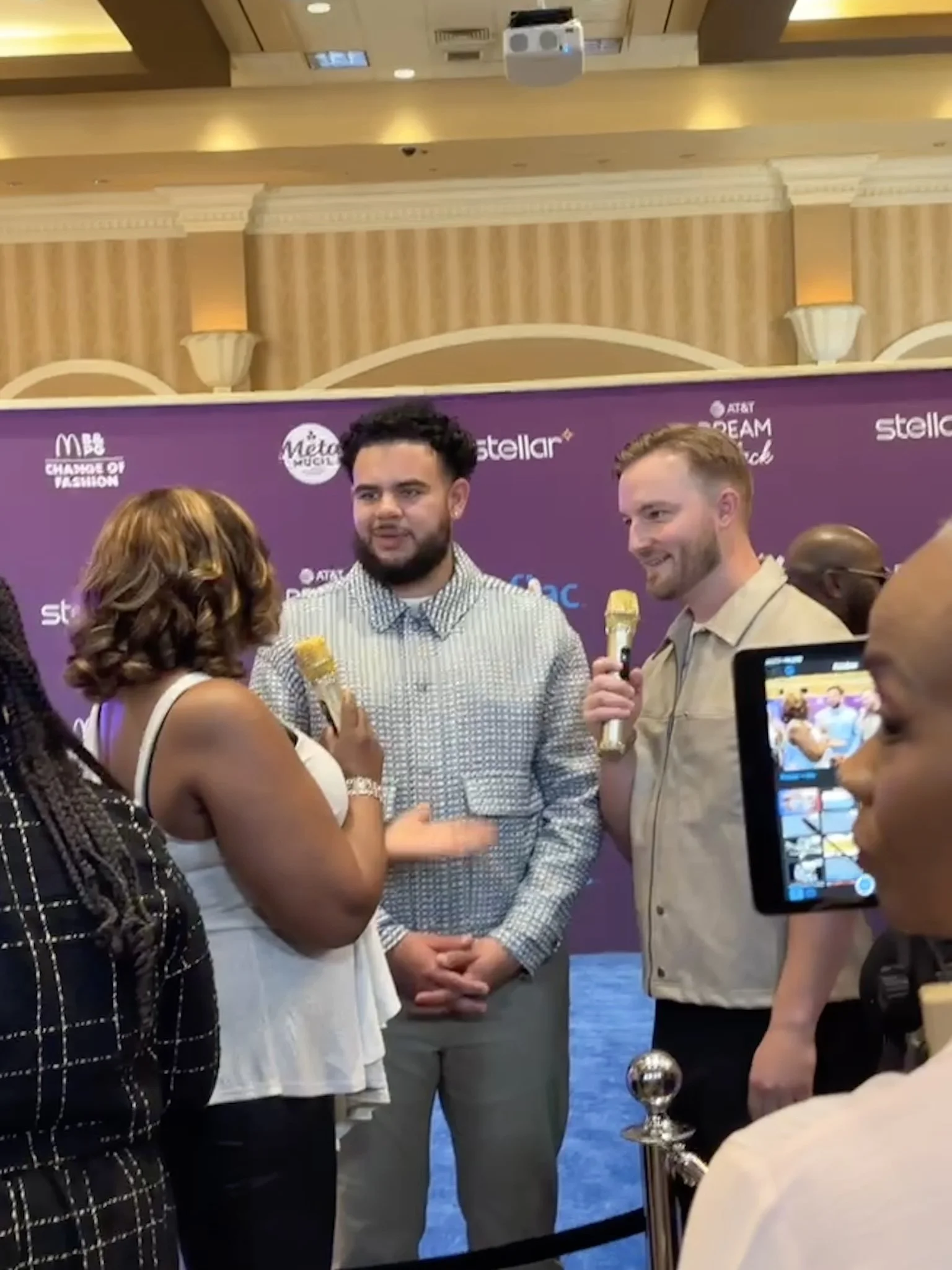 Two men being interviewed by a woman holding a microphone at a press event with a purple backdrop that has various logos including AT&T, Stellar, and others.