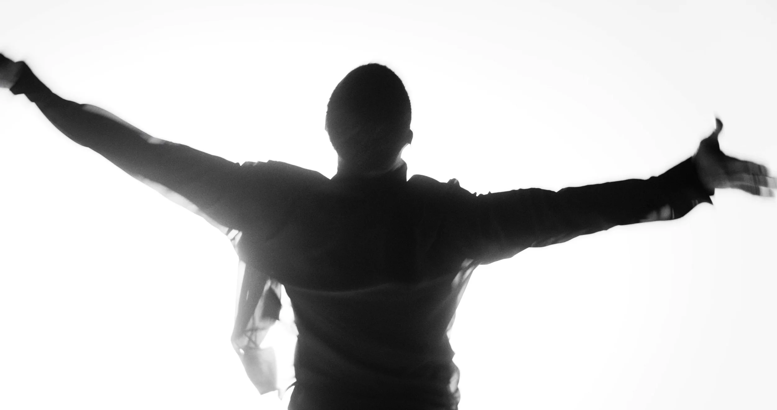 Silhouette of a person with arms raised, standing against a bright background, conveying a sense of freedom or celebration.