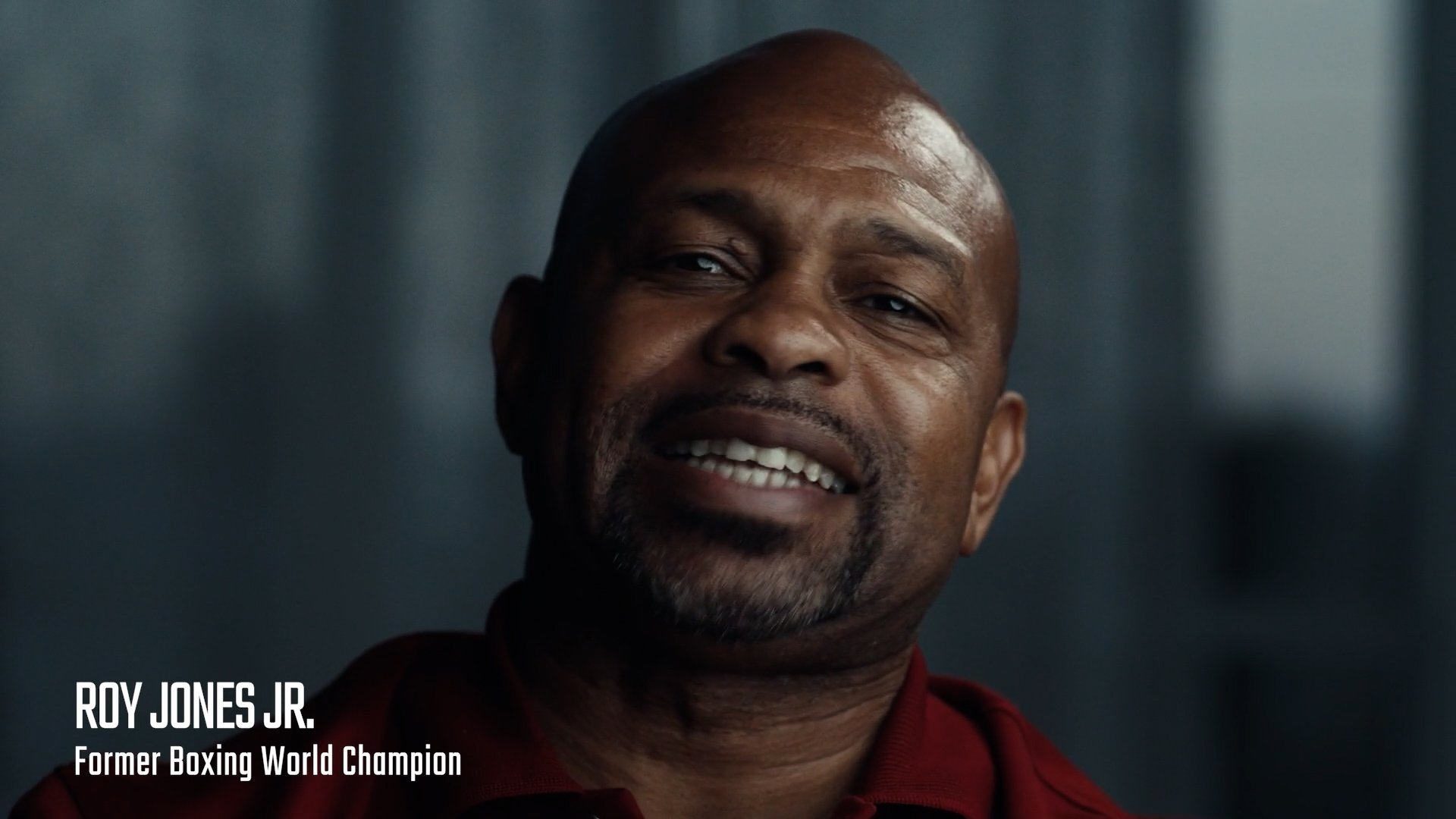 Close-up of Roy Jones Jr., a retired professional boxer and former boxing world champion, wearing a red shirt, smiling softly.