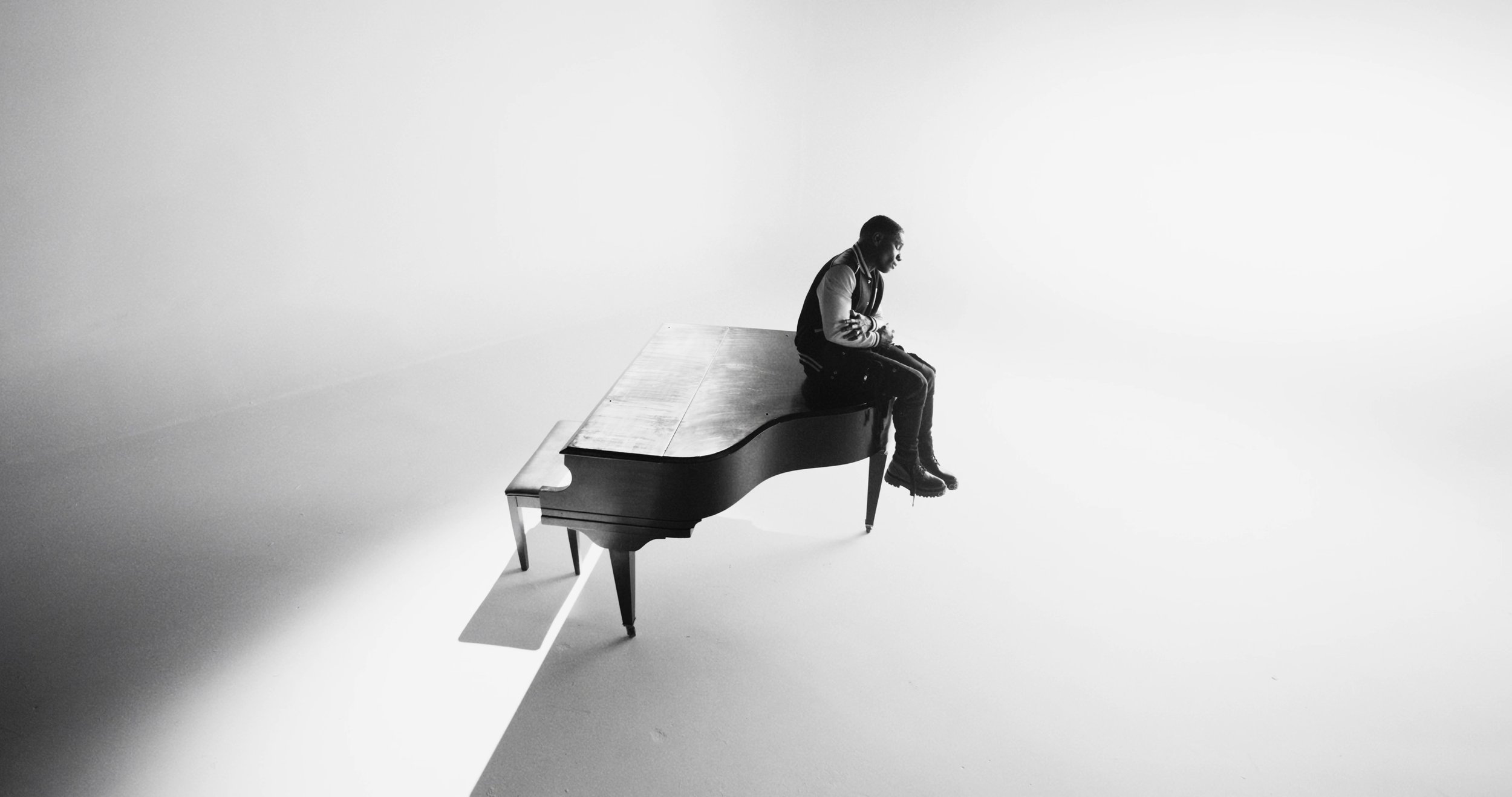 A man sitting alone on a grand piano in a minimalist, white space.