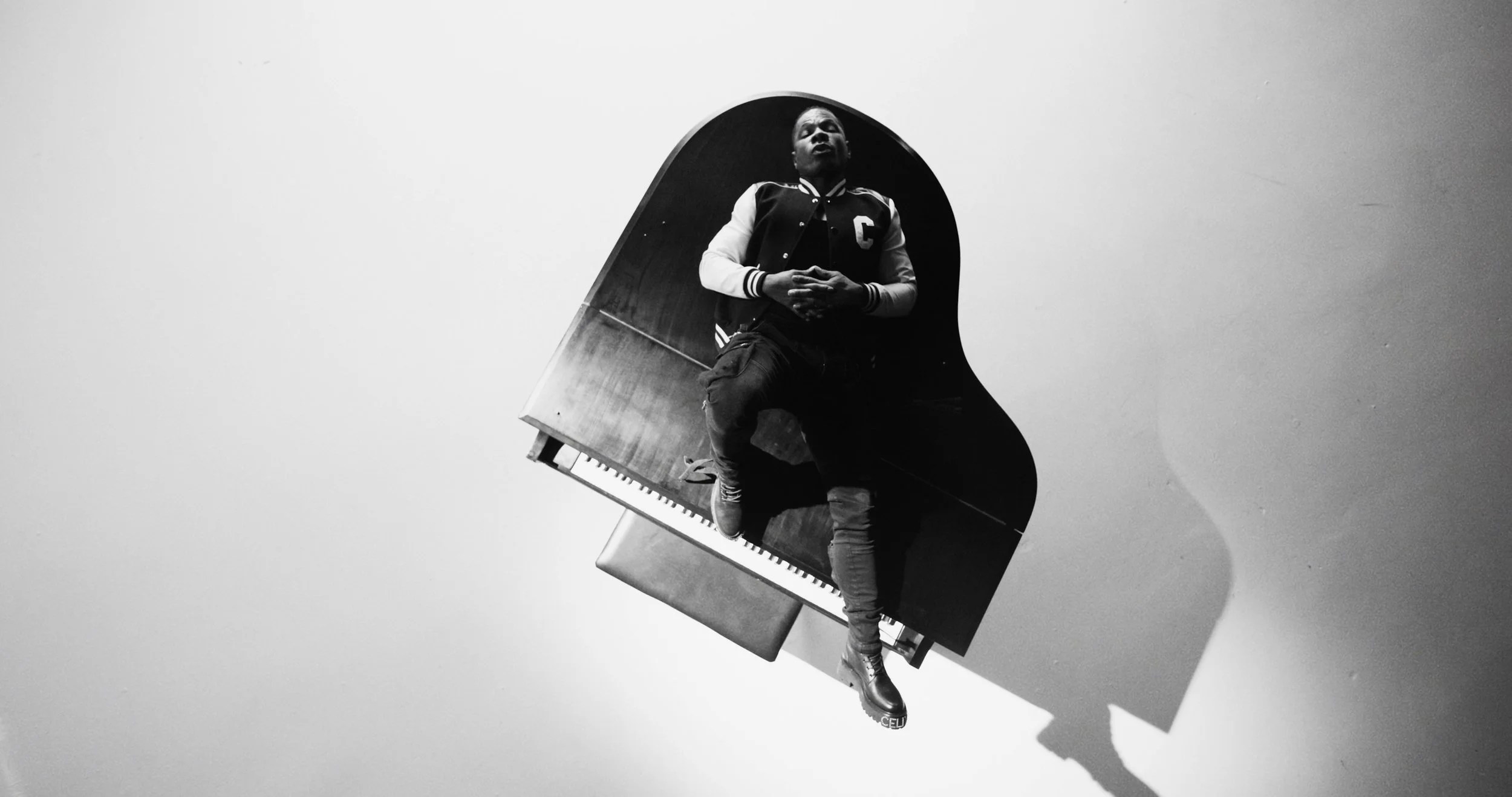 A person sitting on top of a grand piano, viewed from below, in black and white.