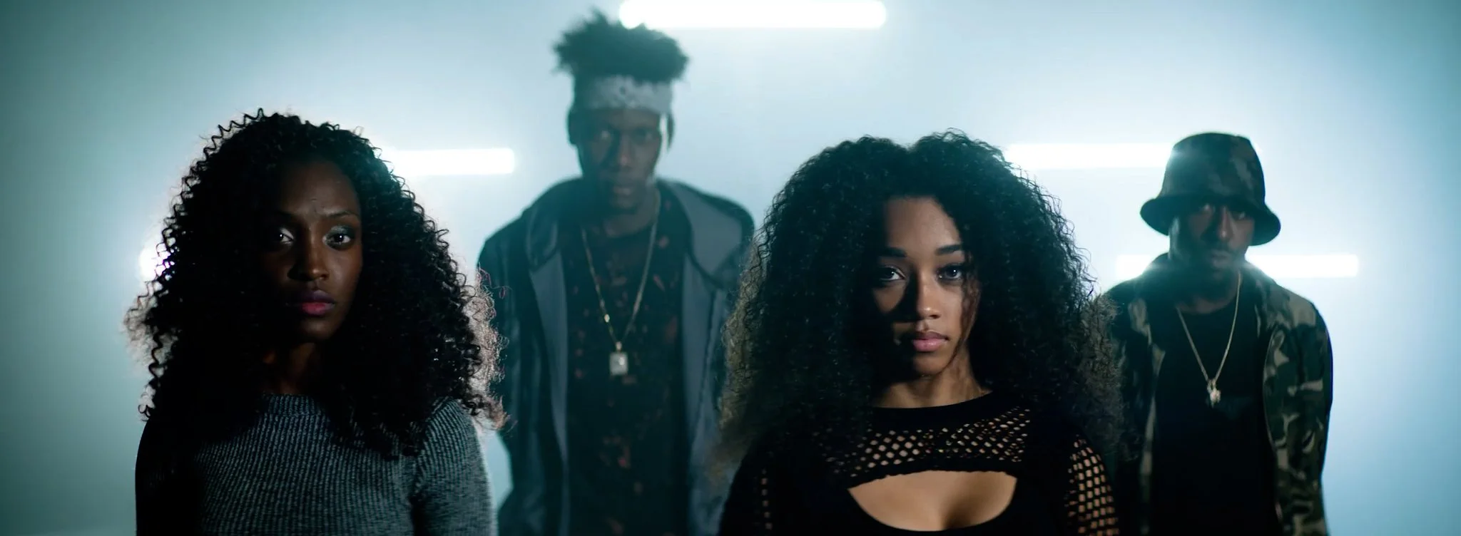 Four young adults with curly hair standing in a dimly lit room with neon lights.