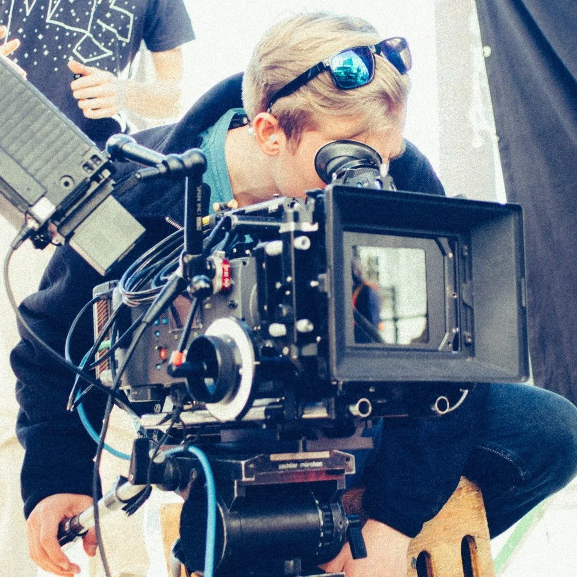 A person operating a professional camera with a viewfinder, wearing sunglasses on their head, working on a film or photo shoot.