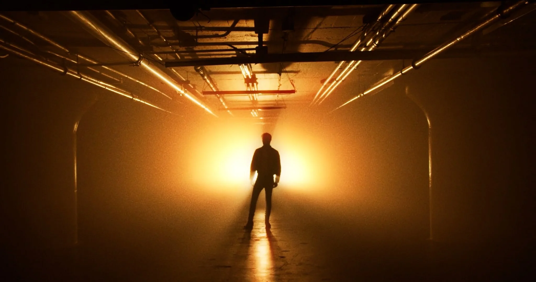 Person standing in a dimly lit tunnel with bright orange light behind them, creating a silhouette effect.