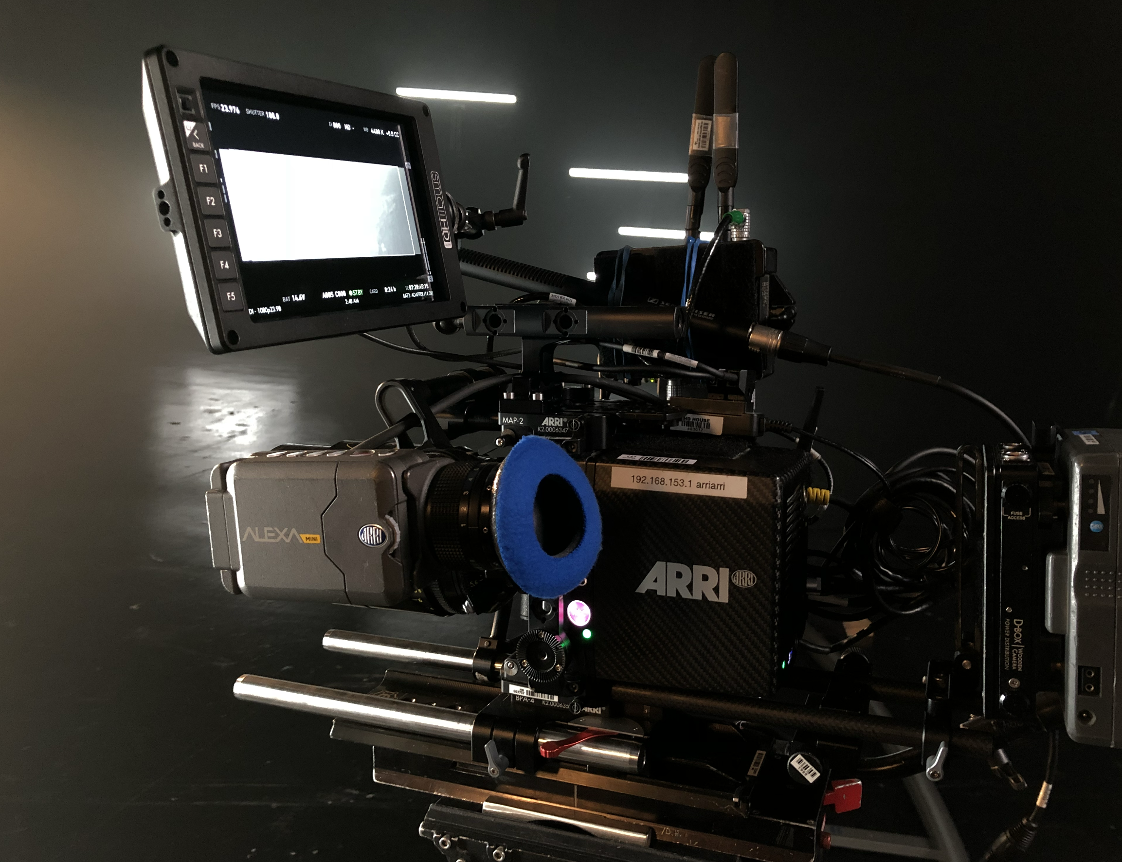 A professional RED digital cinema camera with a mounted monitor, mounted on a rig with various cables and accessories, set against a dark background.