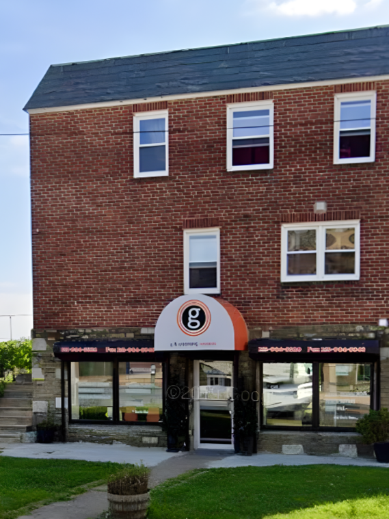 Brick building with a storefront on the ground level, featuring large windows and an arched sign with a lowercase 'g' logo, above the entrance.