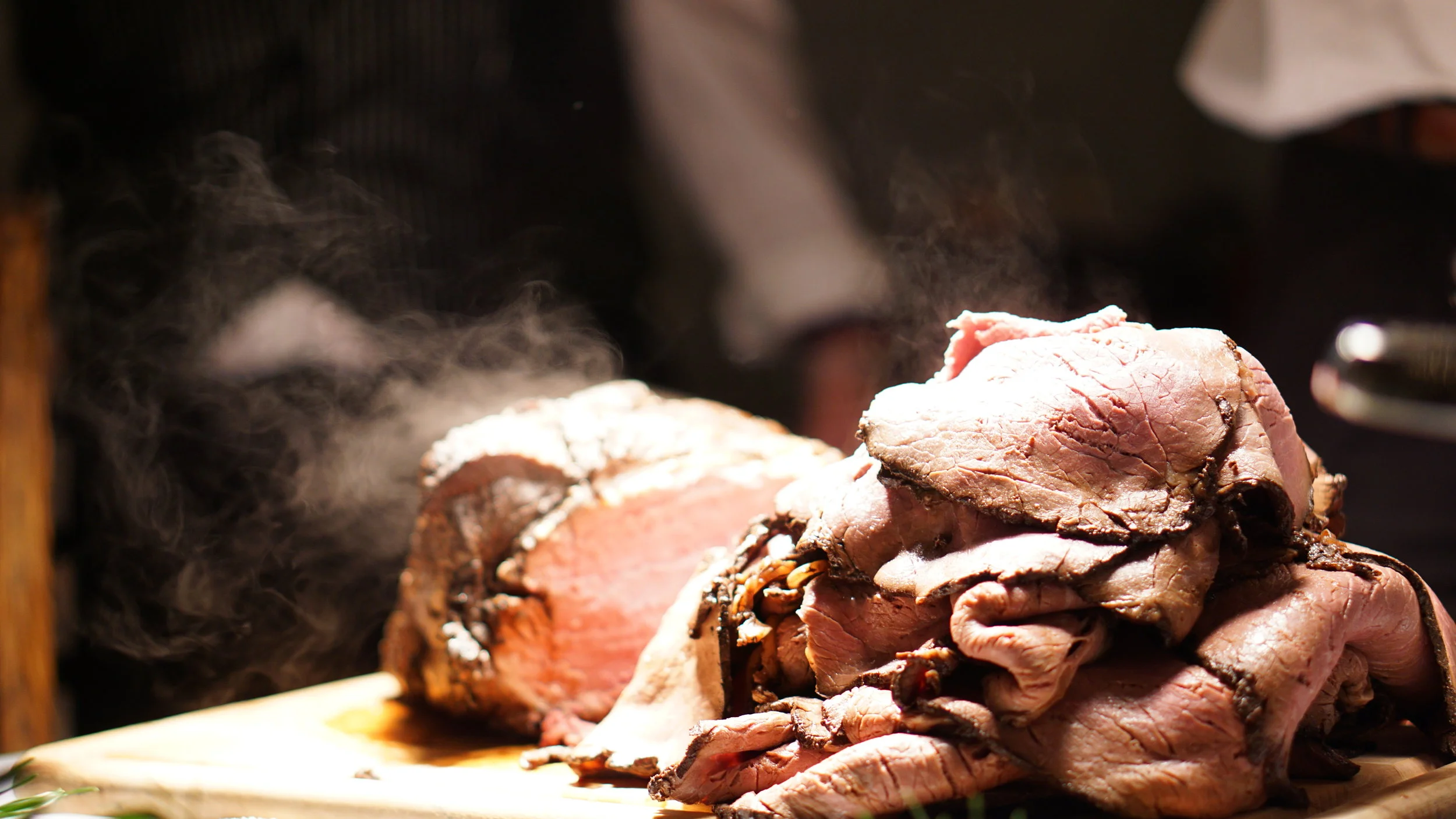 Smoked and cooked slices of beef on a cutting board with steam rising from the meat.