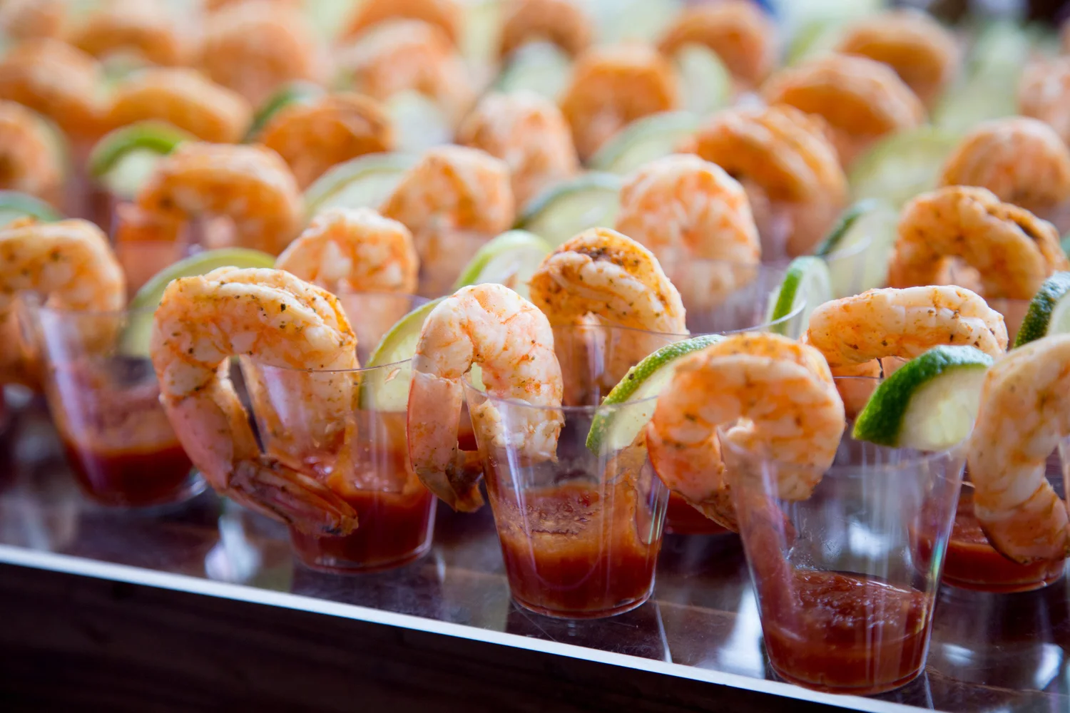 Seafood cocktail appetizers with shrimp, lime wedges, and sauce in clear cups.