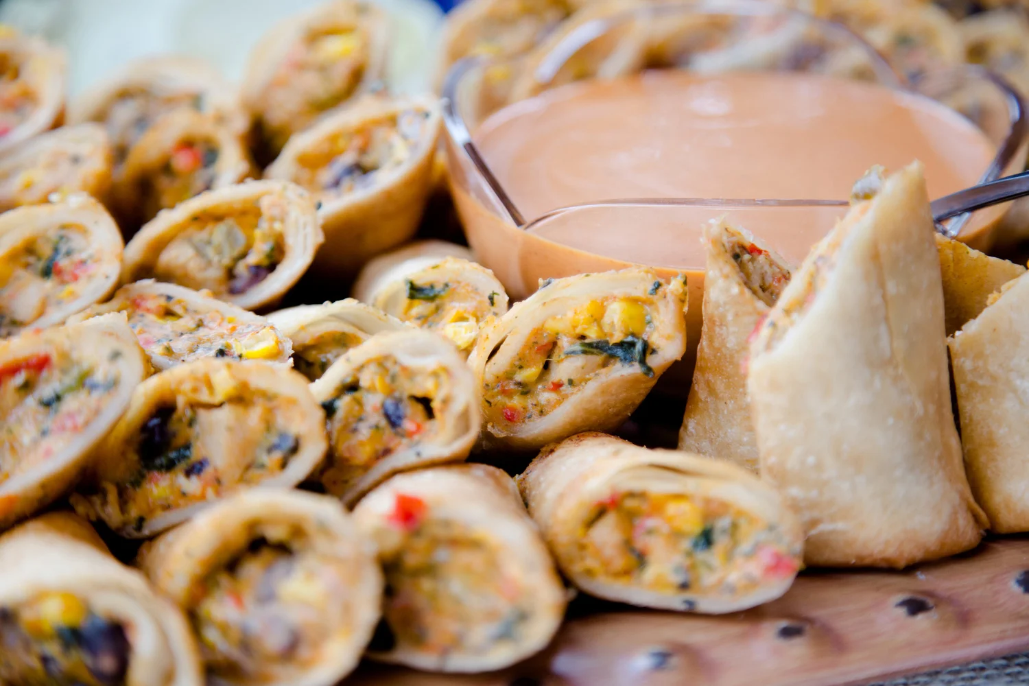 Mini spring rolls with vegetable filling surrounding a bowl of dipping sauce.