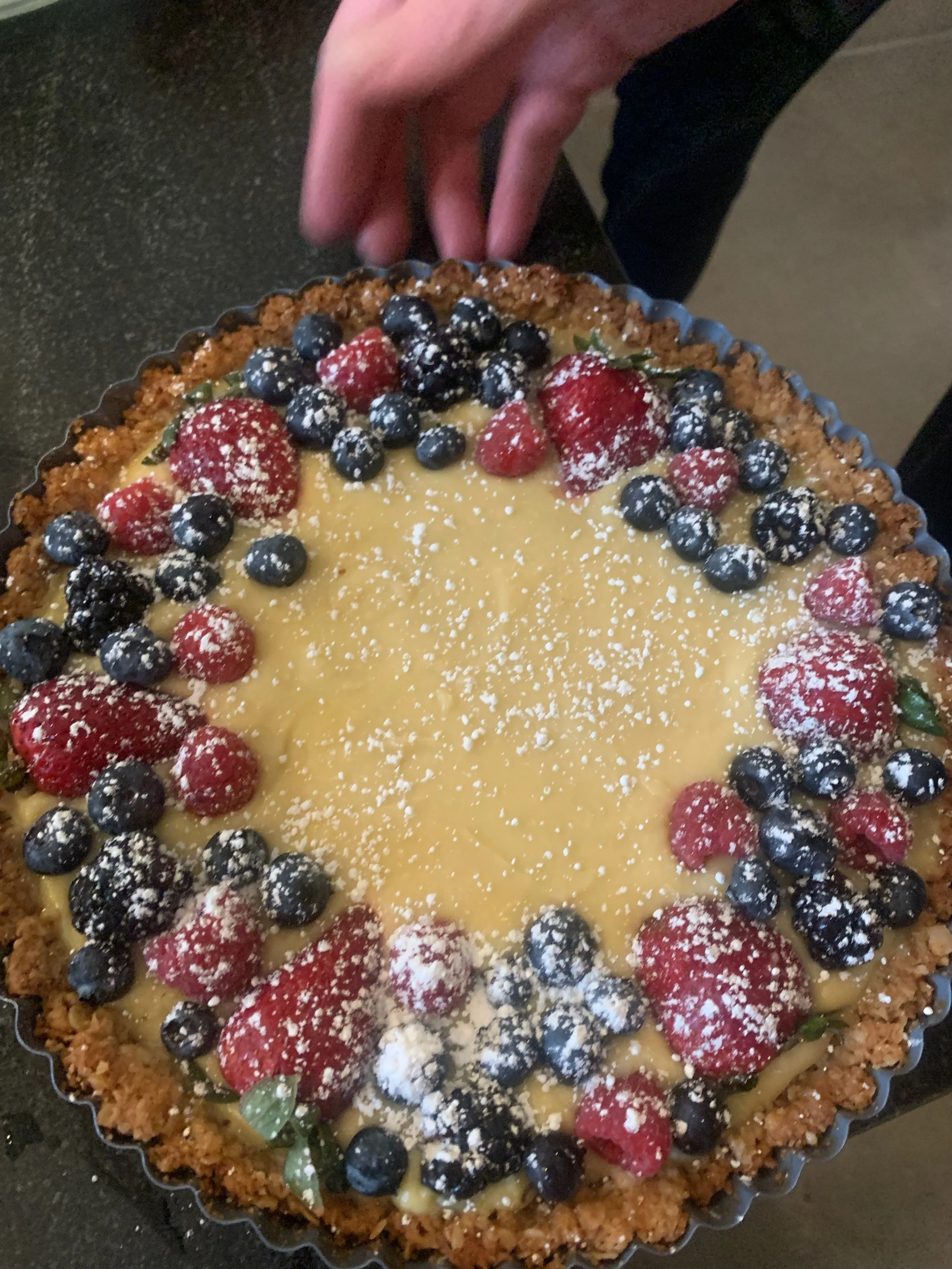 A fruit tart with a pastry crust, filled with custard and topped with strawberries, blueberries, and blackberries, dusted with powdered sugar.