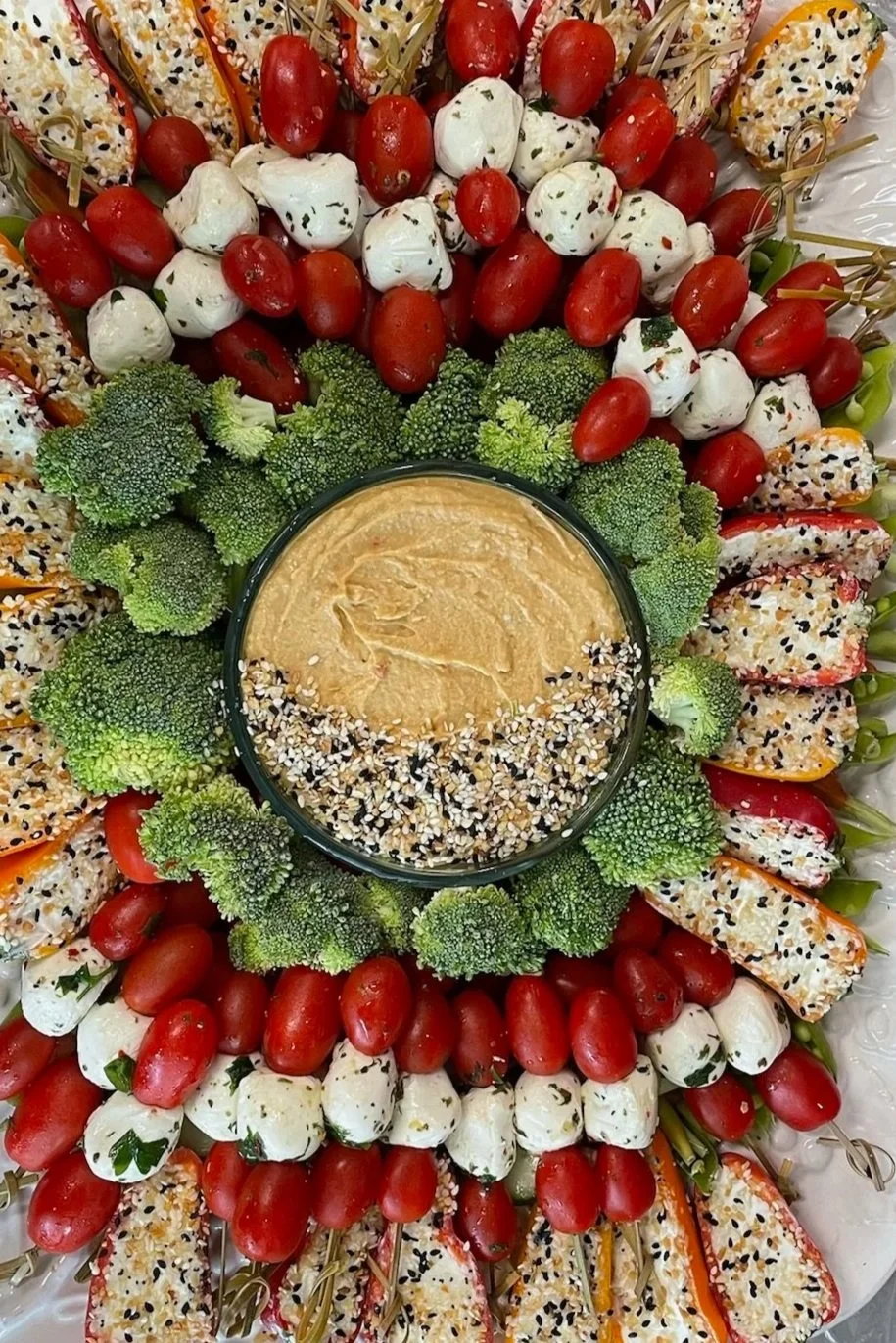 A platter of assorted fresh vegetables and cheese balls arranged around a bowl of hummus.