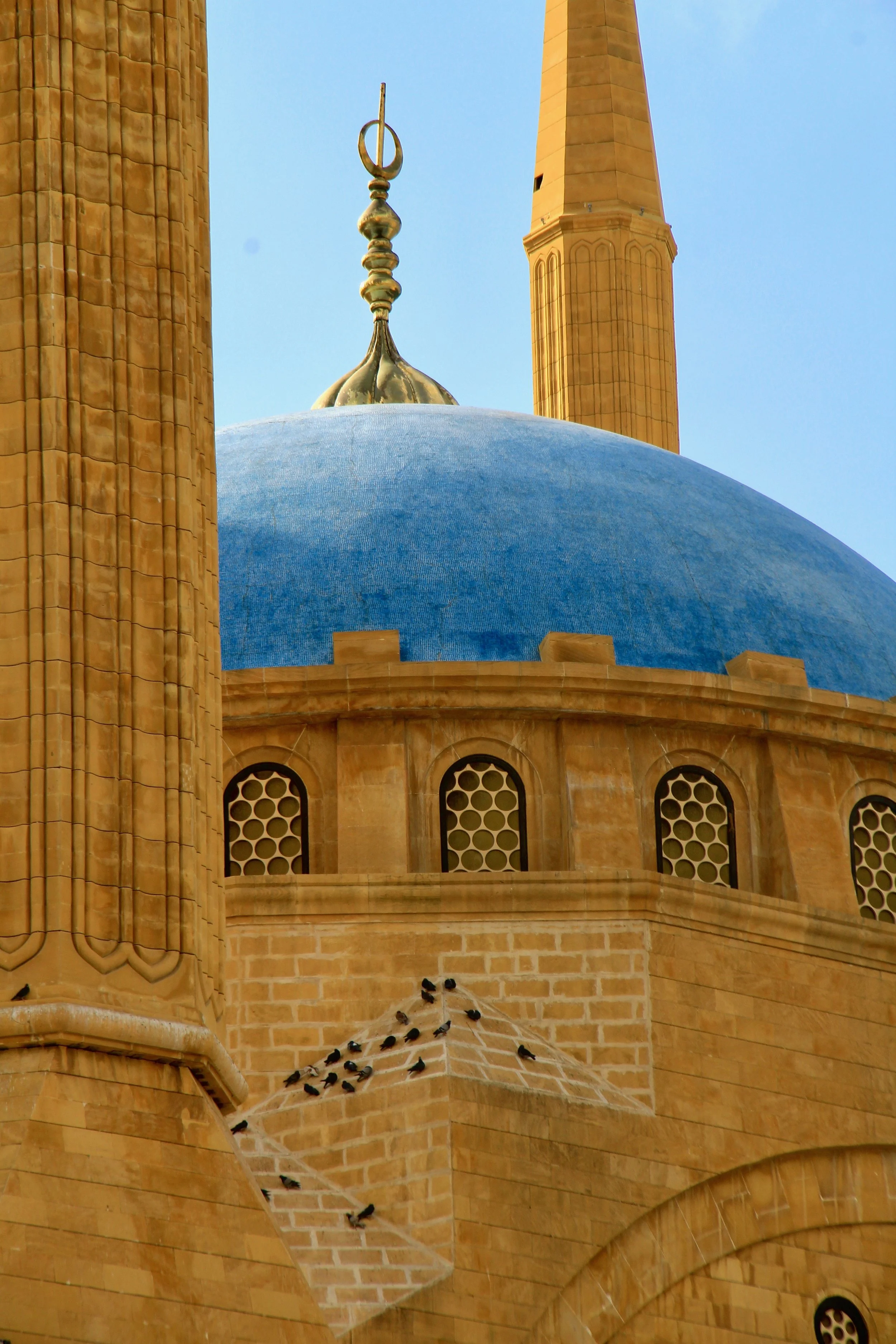 Close-up view of a mosque's blue dome, with two tall minarets and a flock of birds resting on the brick wall.