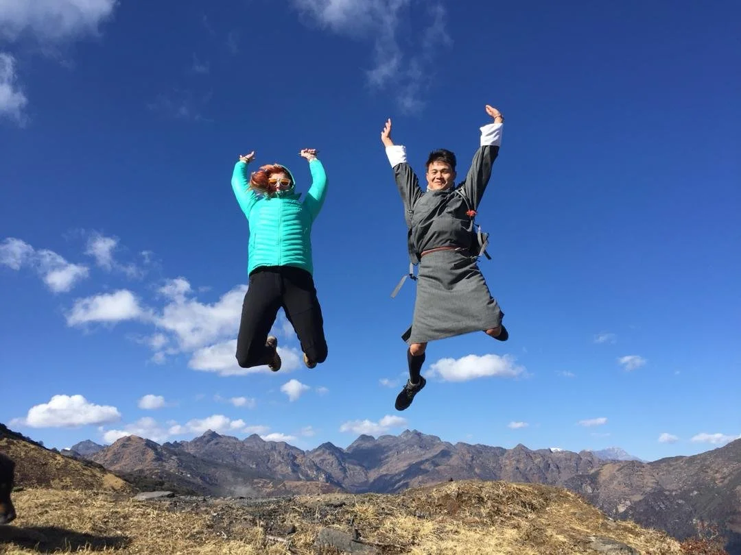 Two people jumping in the air on a mountain landscape with clear blue sky and some clouds.