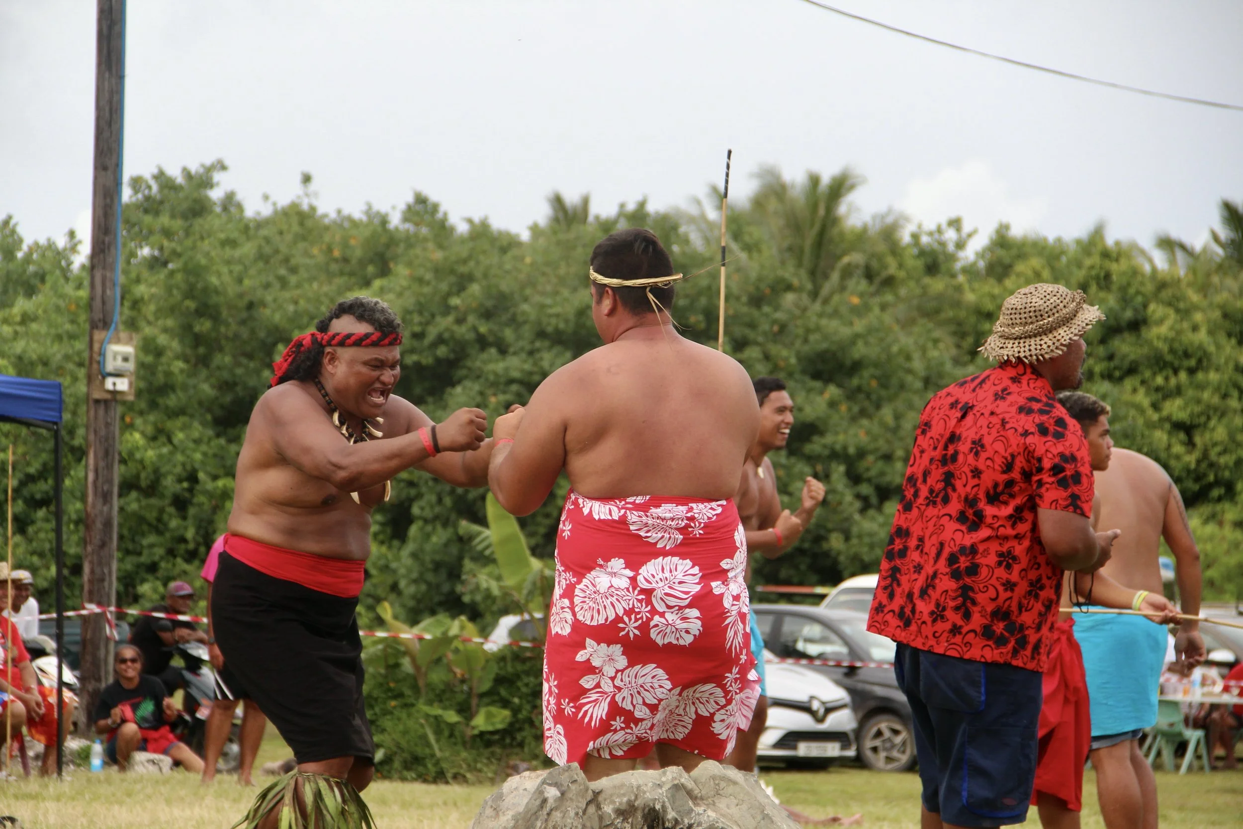 Indigenous people dancing and celebrating outdoors, dressed in traditional clothing and accessories.