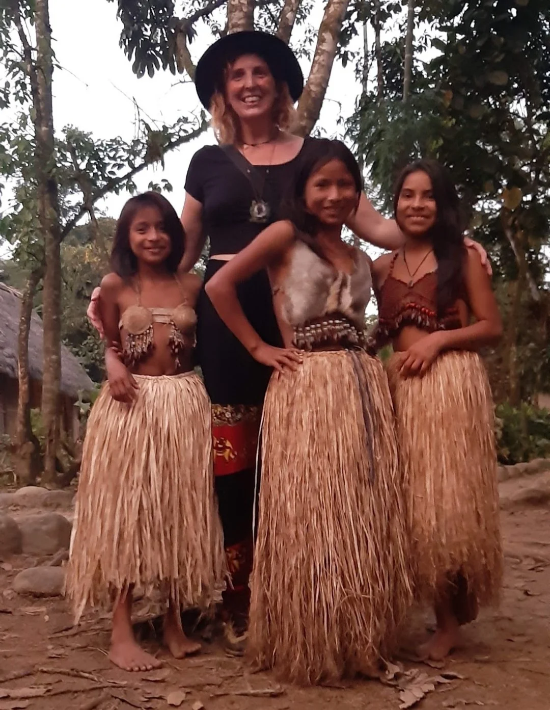 A woman and three girls in traditional tribal attire standing outdoors near trees.