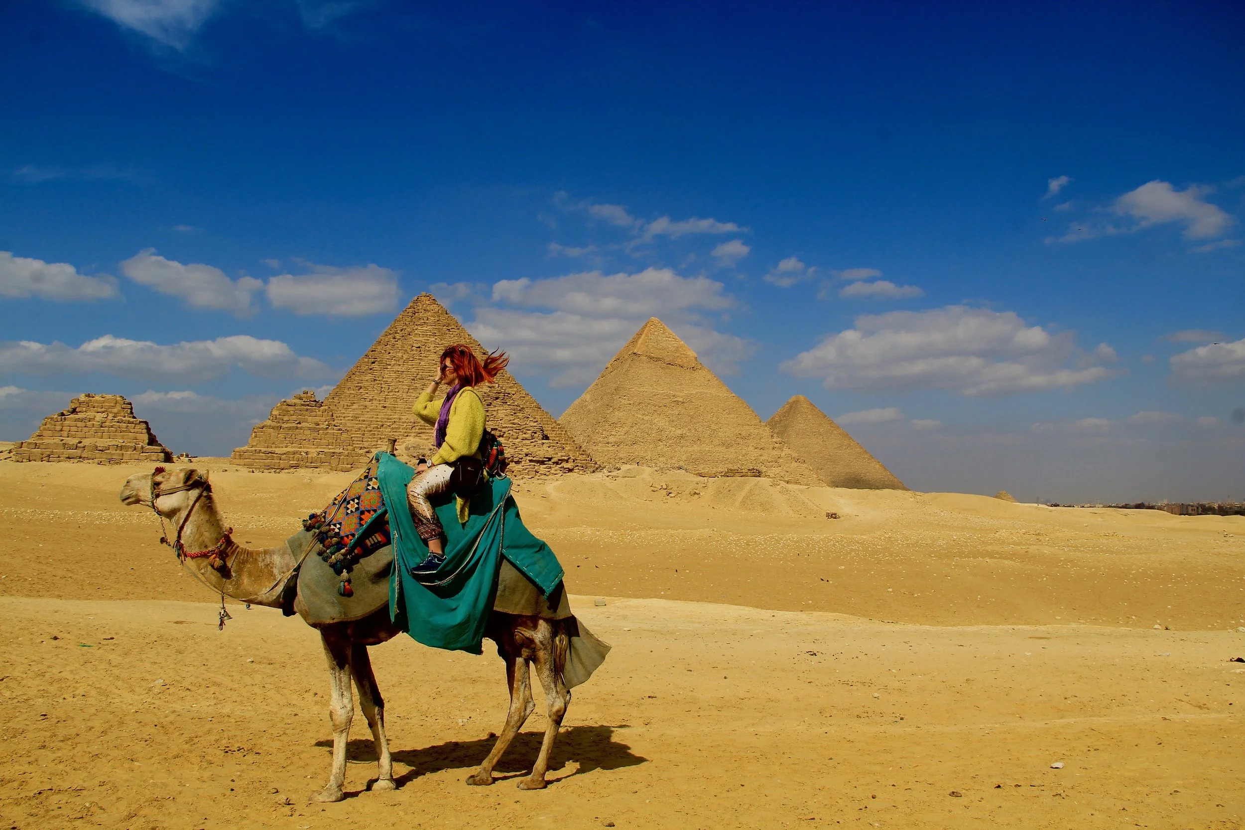 A woman riding a camel in front of the pyramids in Egypt on a sunny day.