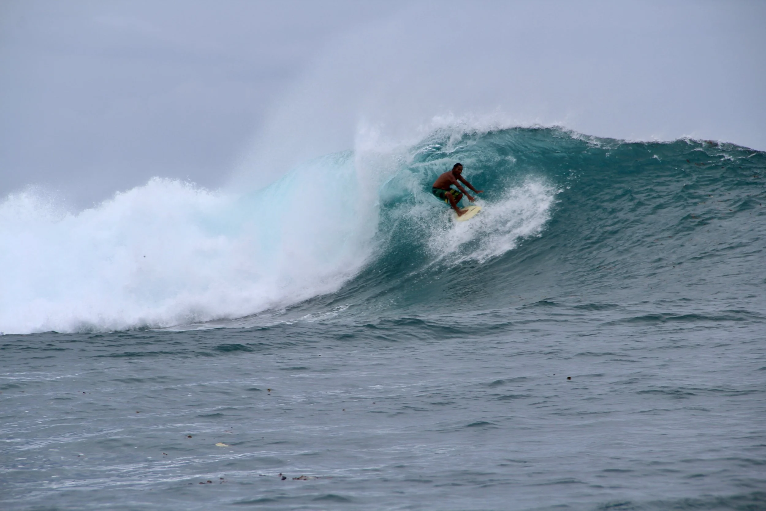 A person surfing on a large blue wave in the ocean.