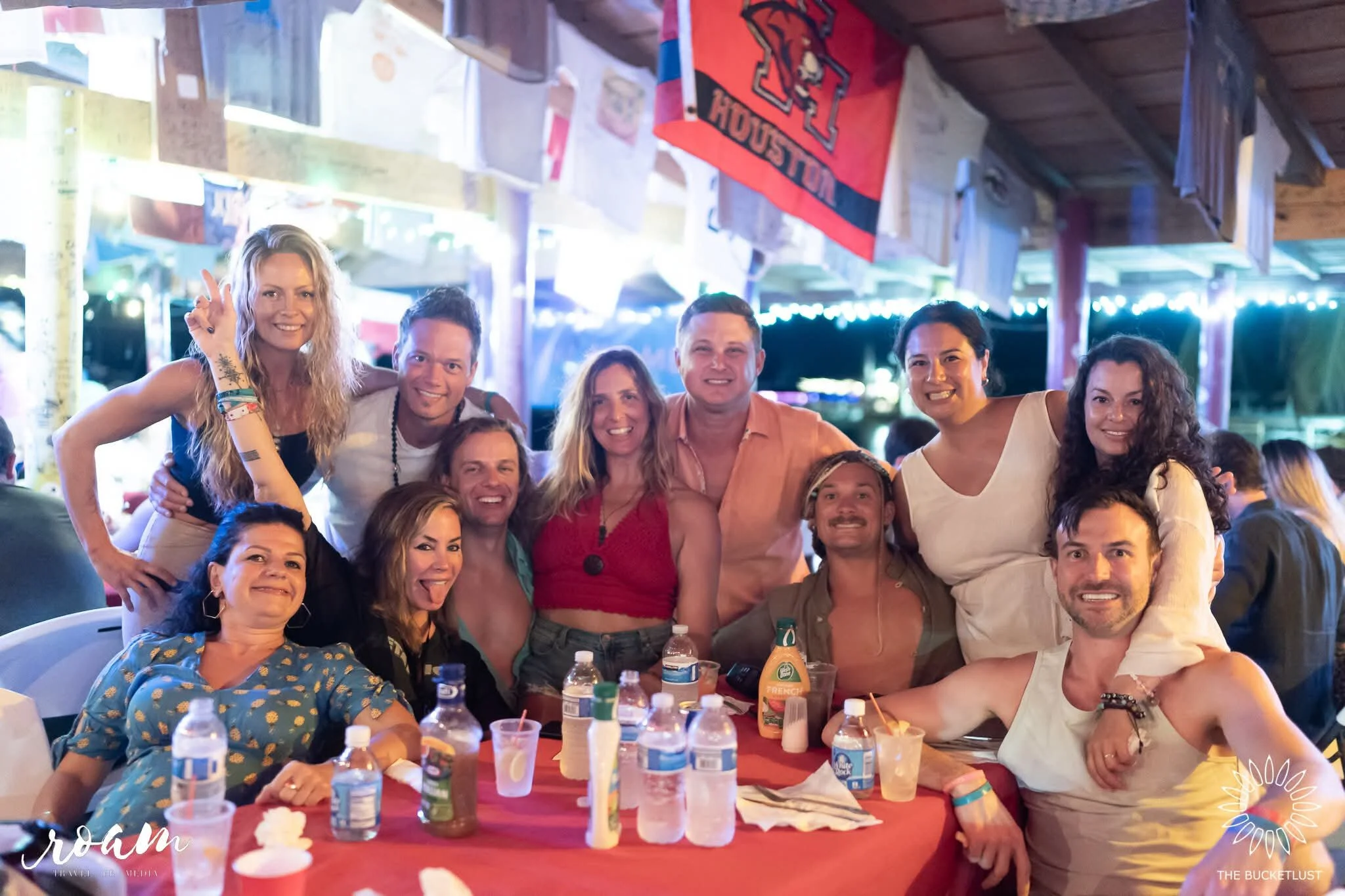 Group of friends enjoying a gathering at a restaurant or bar with decorations and flags hanging from the ceiling, smiling and posing for the photo.