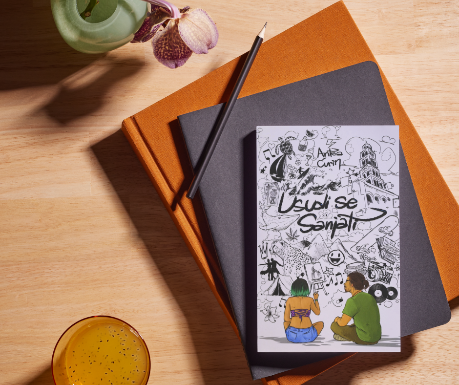A wooden desk with a potted orchid, a glass of orange juice, two stacked notebooks, and a drawing on paper showing two people sitting and sketching, surrounded by cartoon-style doodles.