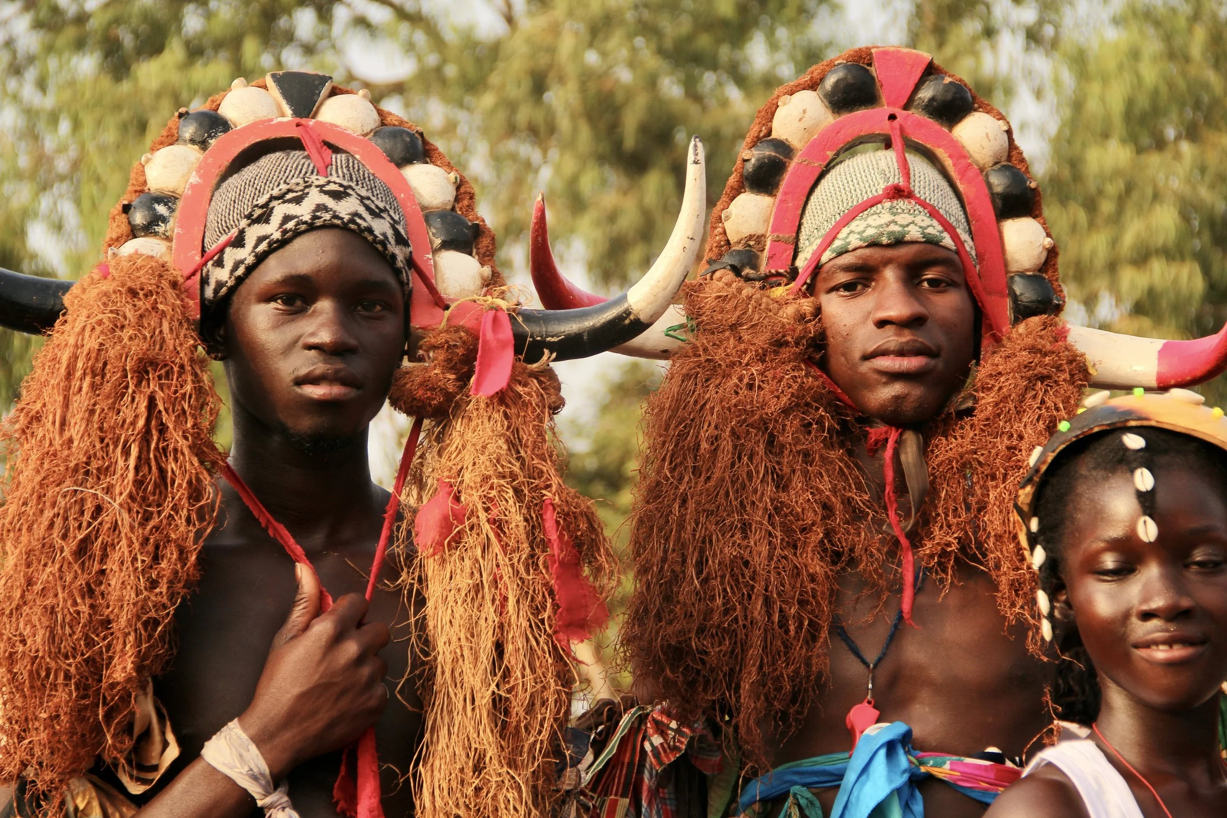 Two men and a woman in traditional tribal costumes and headdresses, standing outdoors during daytime.